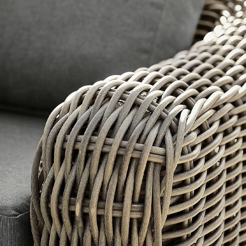 Nahaufnahme einer braunen, geflochtenen Polyrattan-Armlehne an einem Gartenmöbel mit grauem Kissen