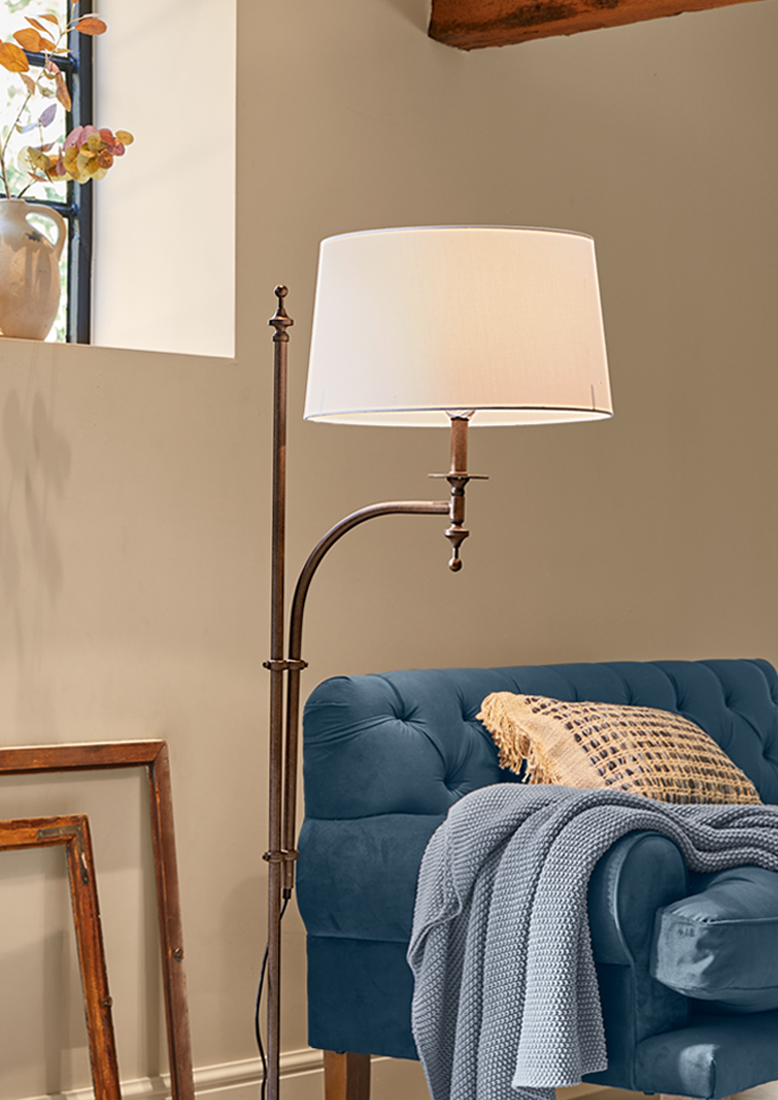 Stehlampe mit Metallgestell und weissem Lampenschirm neben blauem Sofa mit Strickdecke