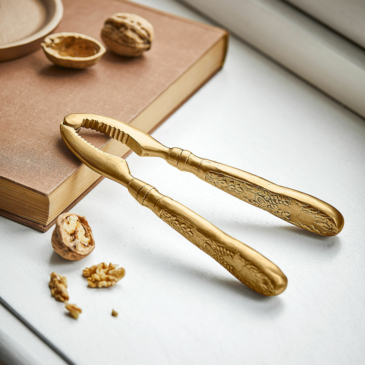 Nussknacker Solenna Goldfarbener Metallnussknacker mit dekorativem Muster an den Griffen auf weissem Untergrund