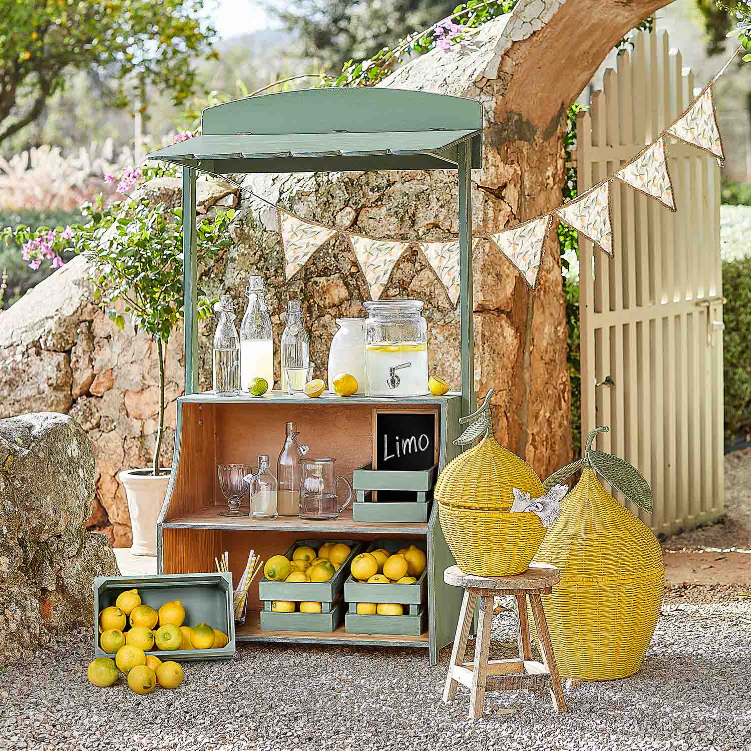 Grüner Holzstand mit Zitronen und Glasflaschen für Limonade in sonnigem Garten