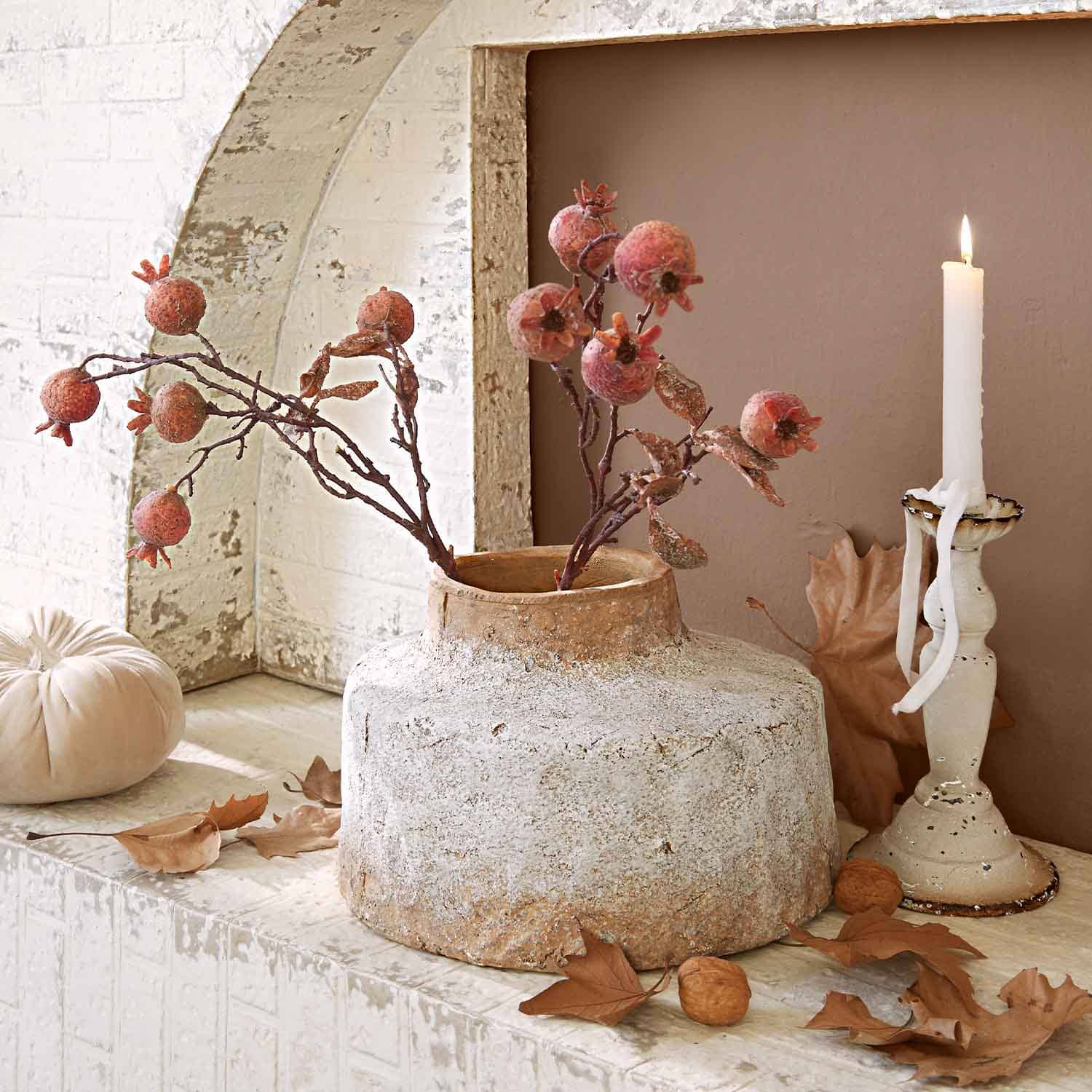 Rustikaler Keramikvase mit Zweigen roter Granatäpfel in warmen Herbstfarben und brennender Kerze