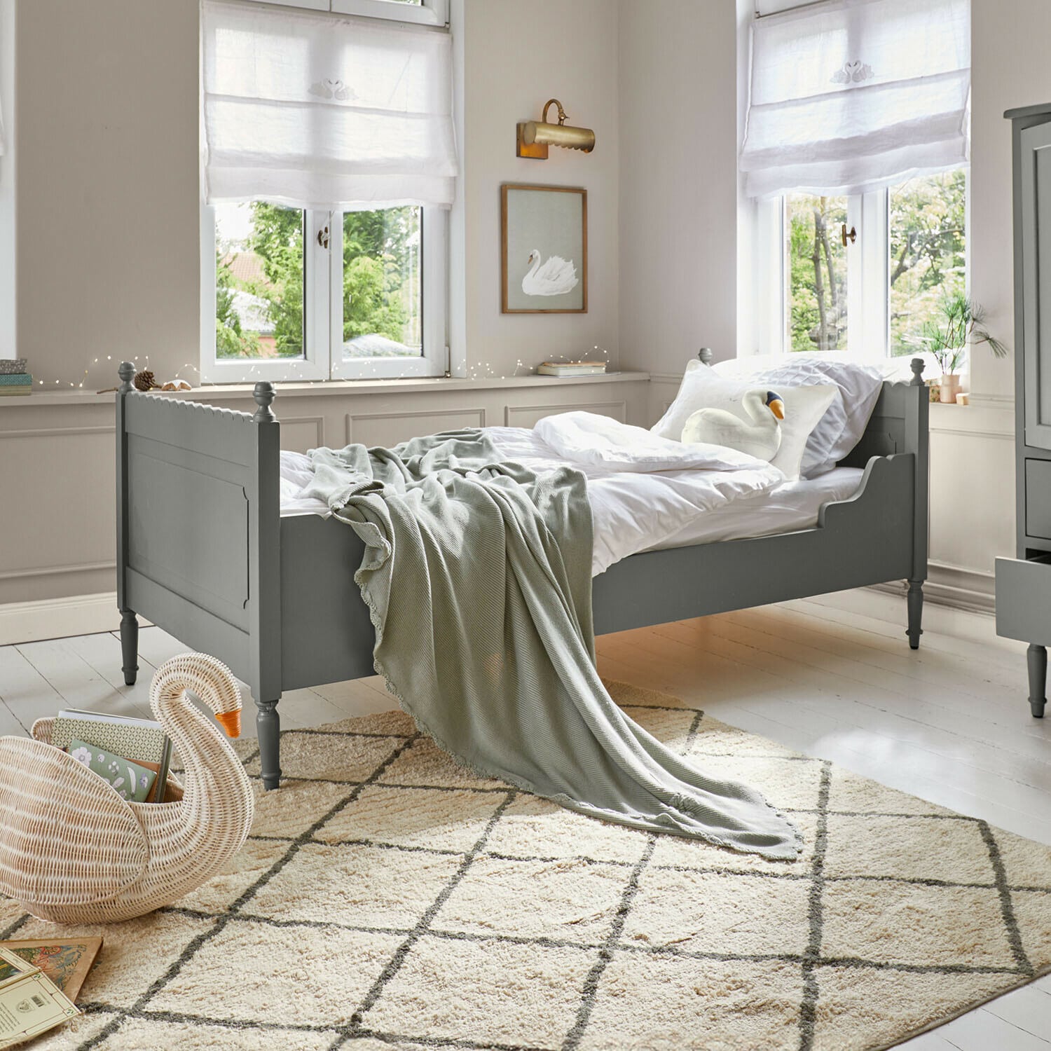 Grünes Holzbett mit weisser Bettwäsche und grauer Decke in hellem Zimmer mit gemustertem Teppich