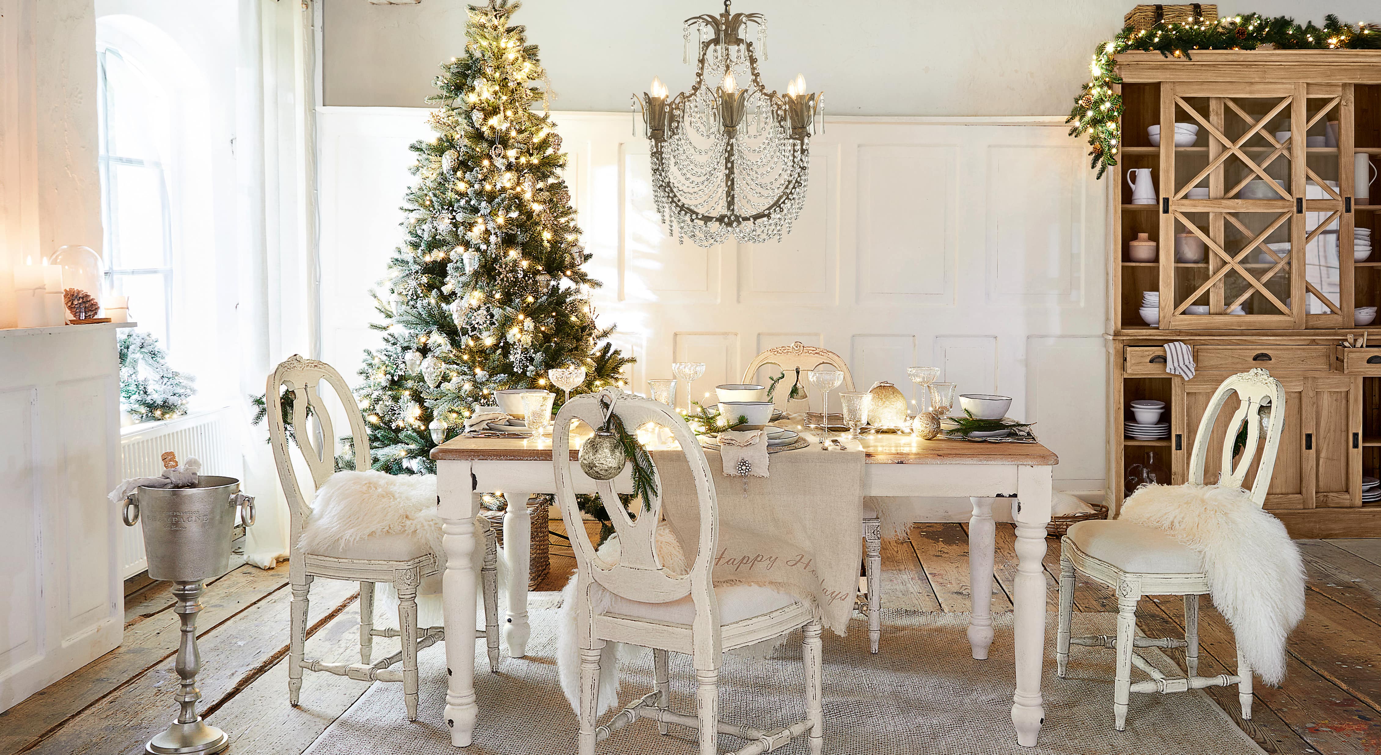 Esszimmer mit weissem Holztisch und Stühlen, festlich dekoriert mit Weihnachtsbaum und Kristallleuchter