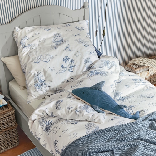 Bettwäsche aus Baumwolle in Weiss mit blauen Meeresmotiven auf grauem Bett mit Haifischkissen
