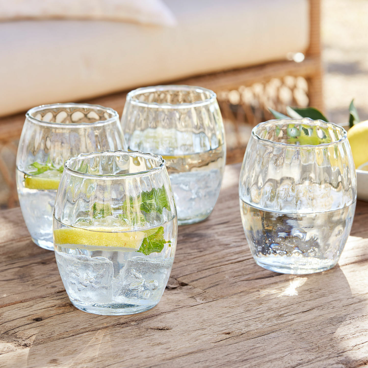 Glas 4er Set Bourgavin Vier Gläser aus klarem Glas mit Wasser, Eis und Zitrone auf einem Holztisch.