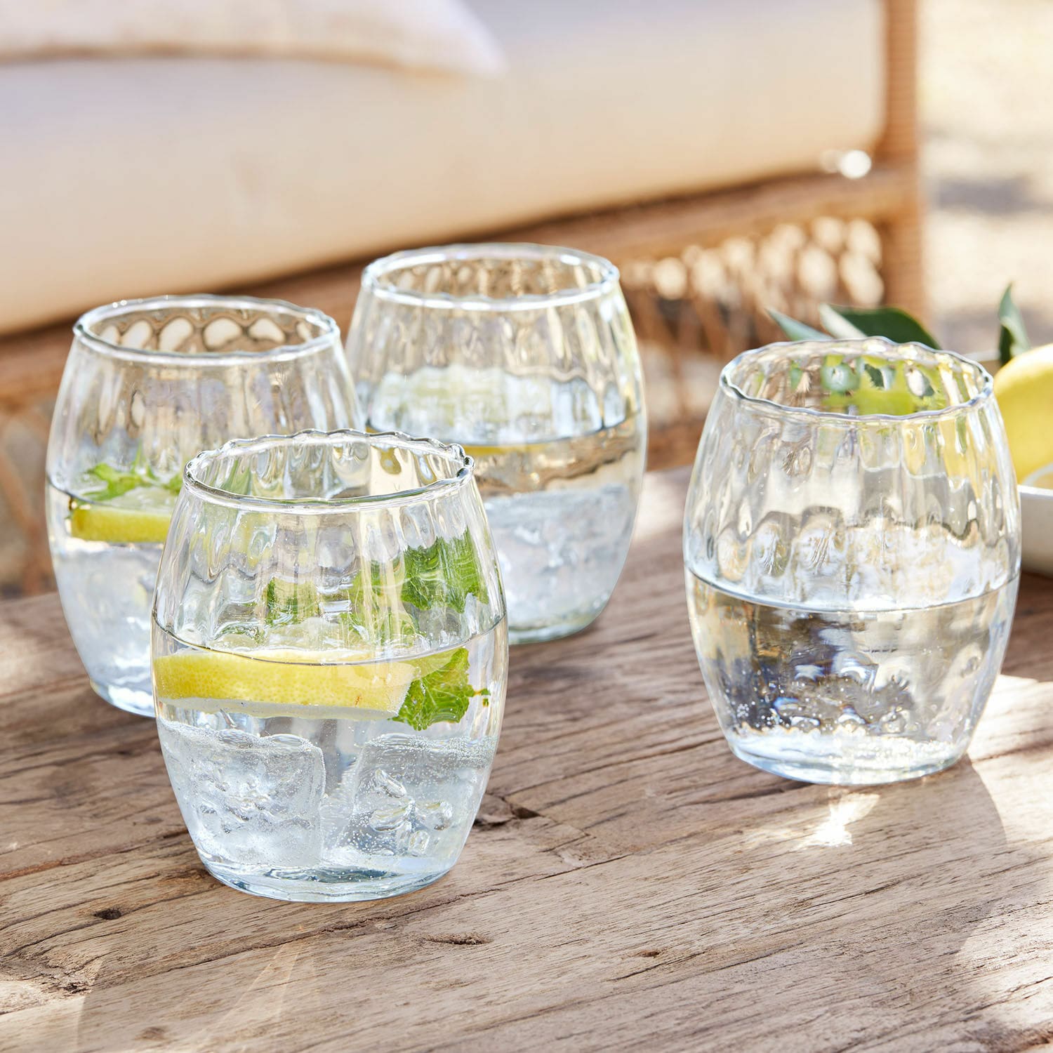 Glas 4er Set Bourgavin Vier Gläser aus klarem Glas mit Wasser, Eis und Zitrone auf einem Holztisch.