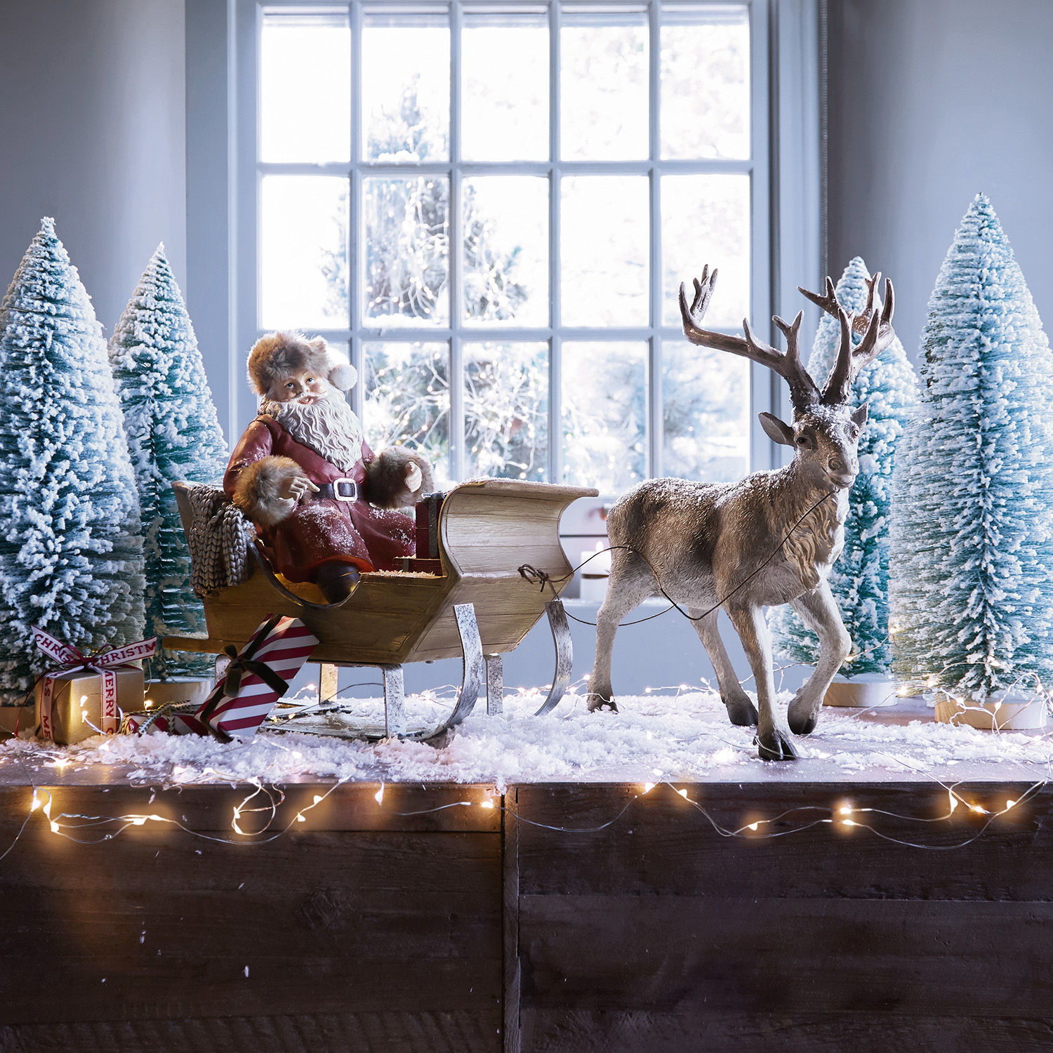 Weihnachtsschlitten Palaima Weihnachtsfigur Santa Claus im roten Mantel auf Holzschlitten mit Rentier und schneebedeckten Tannenbäumen