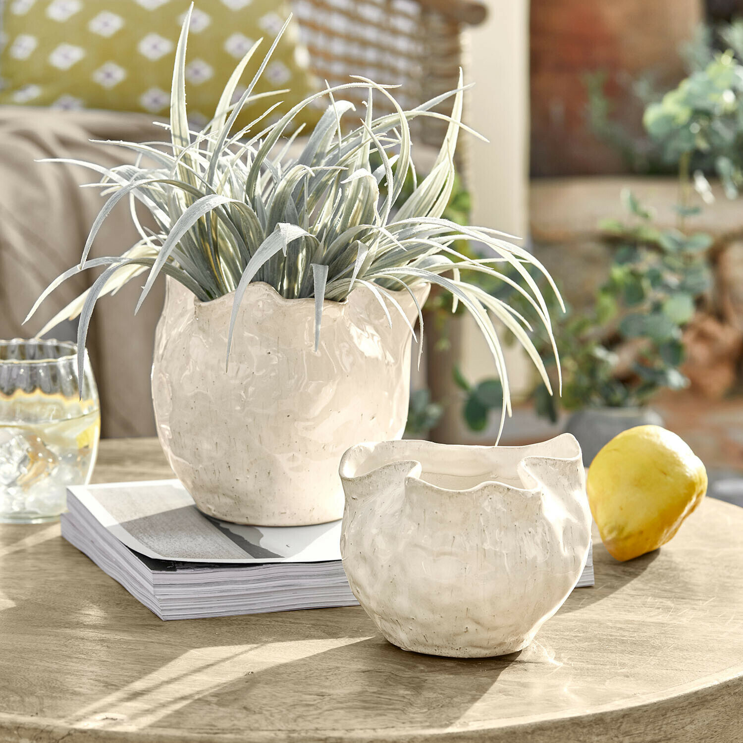 Weiße Keramikblumentöpfe mit unregelmäßiger Form auf Holztisch mit grüner Pflanze und Zitrone