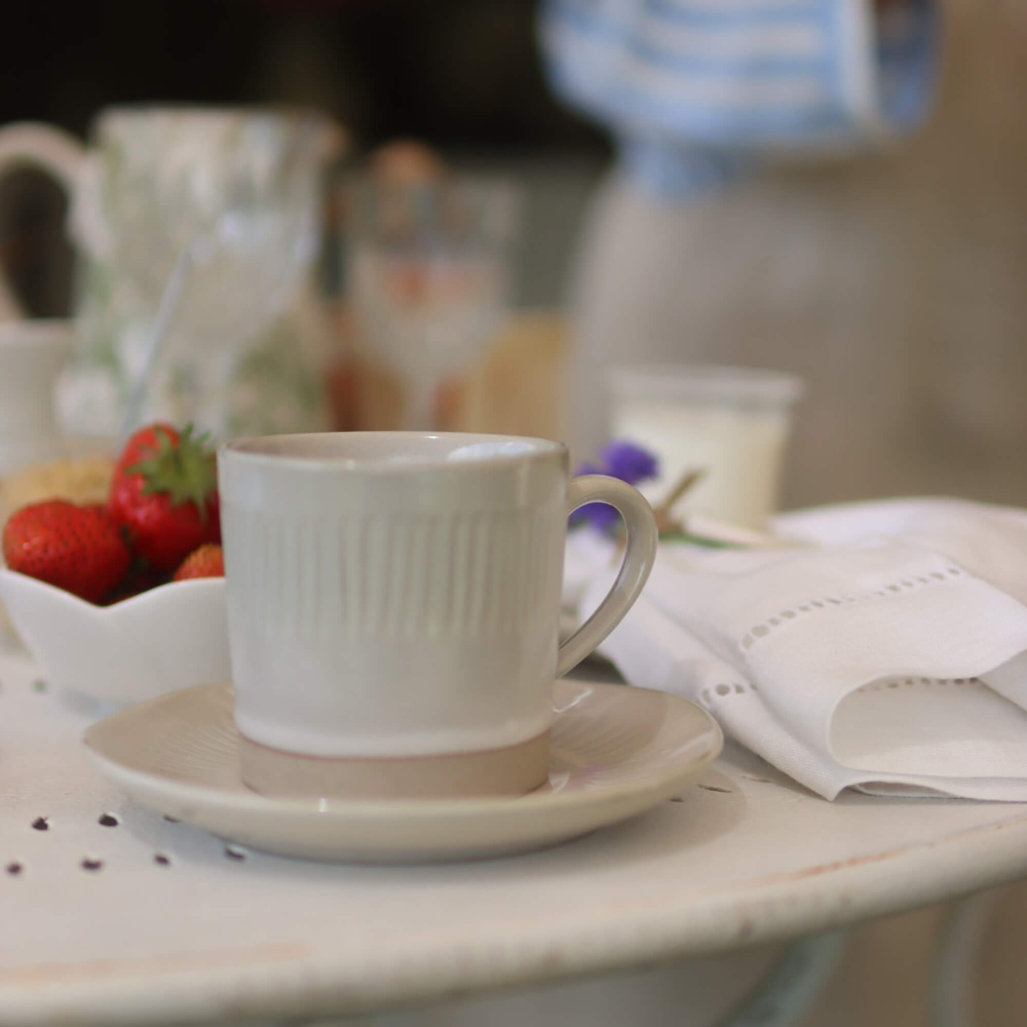 Beige Keramiktasse mit Untertasse auf weissem Tisch mit Erdbeeren und Leinenserviette