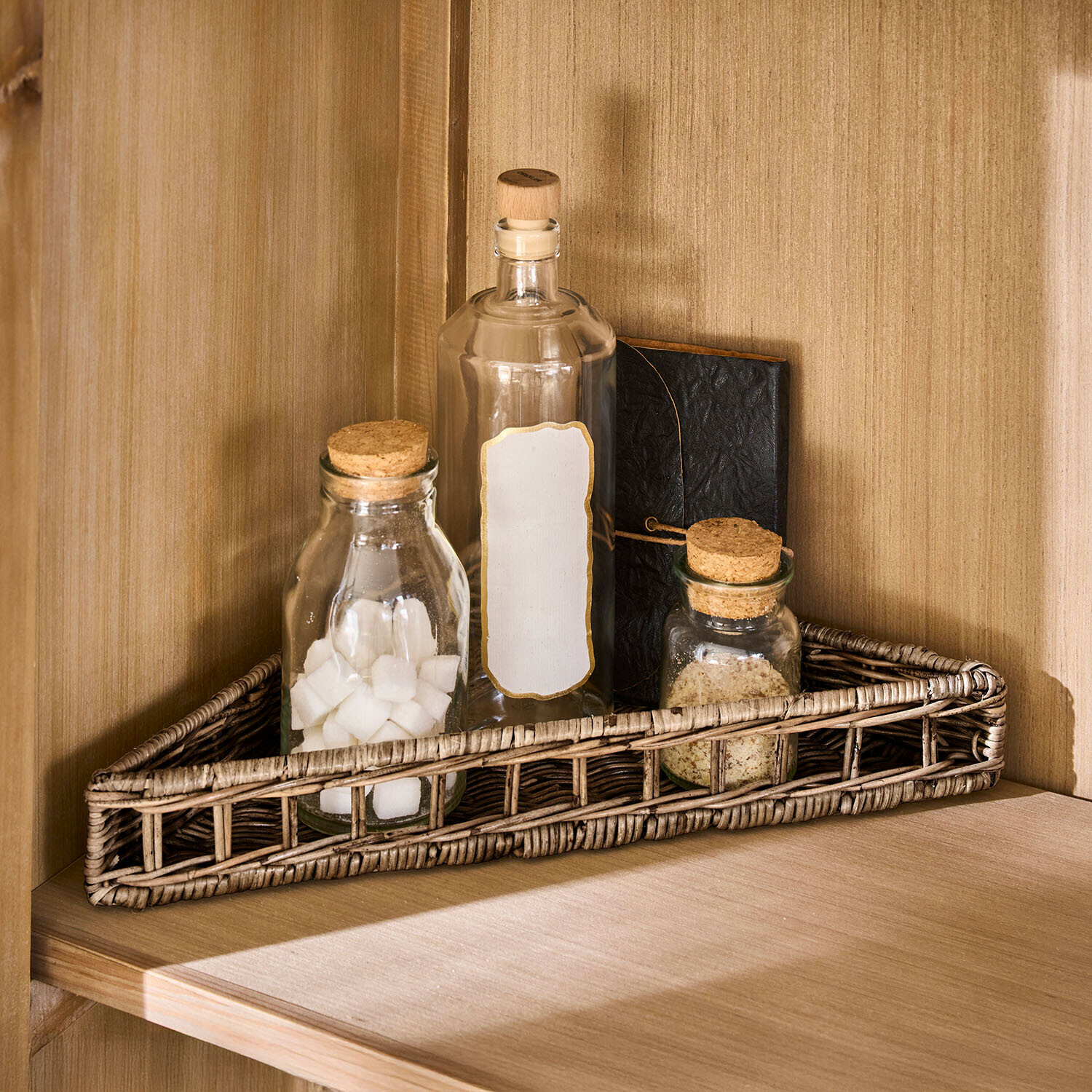 Dreieckiger Rattankorb in Naturfarbe mit drei Glasflaschen und Notizbuch auf Holzregal