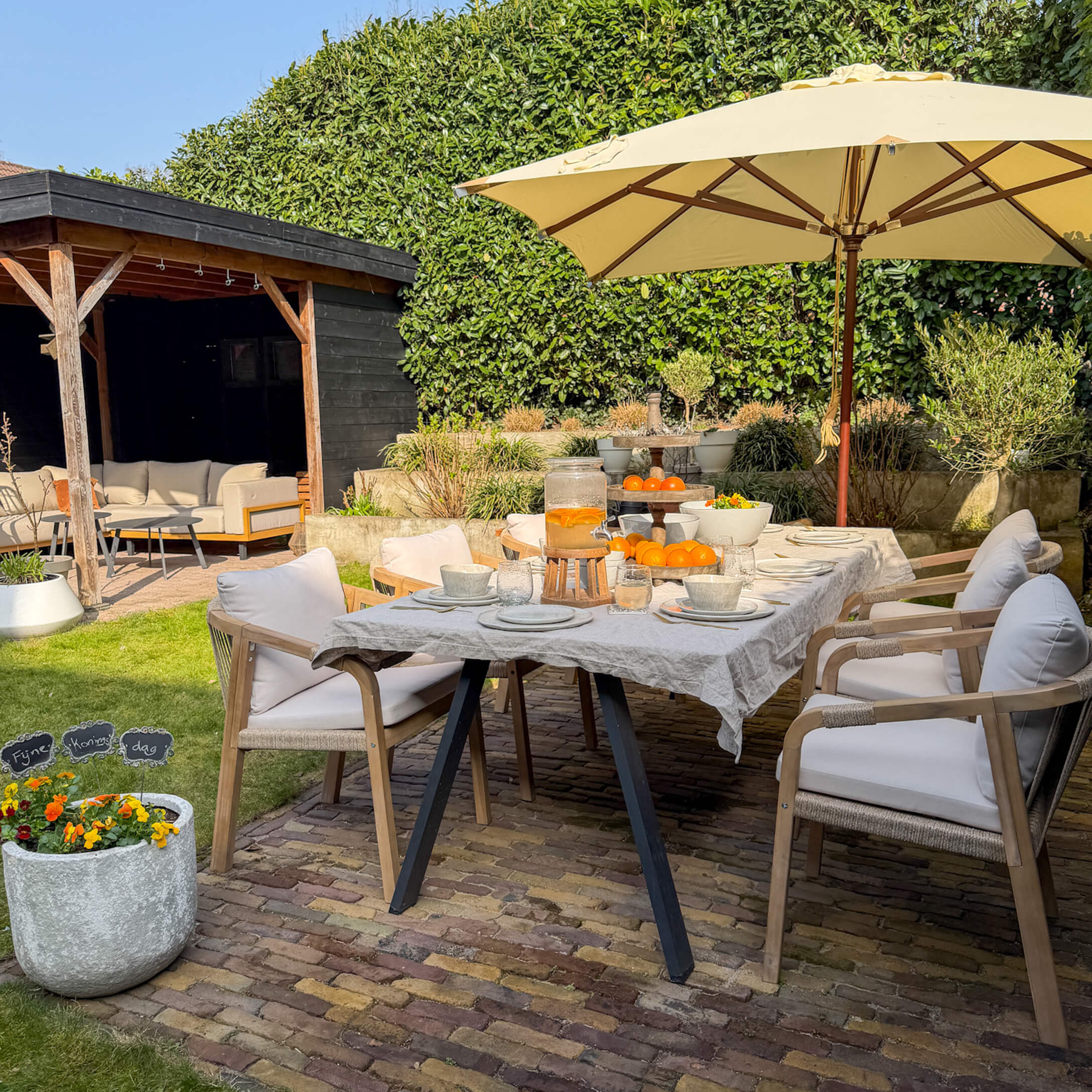 Gartenmöbel mit Holzstühlen und beigem Sonnenschirm auf Steinboden mit Orangen als Dekor