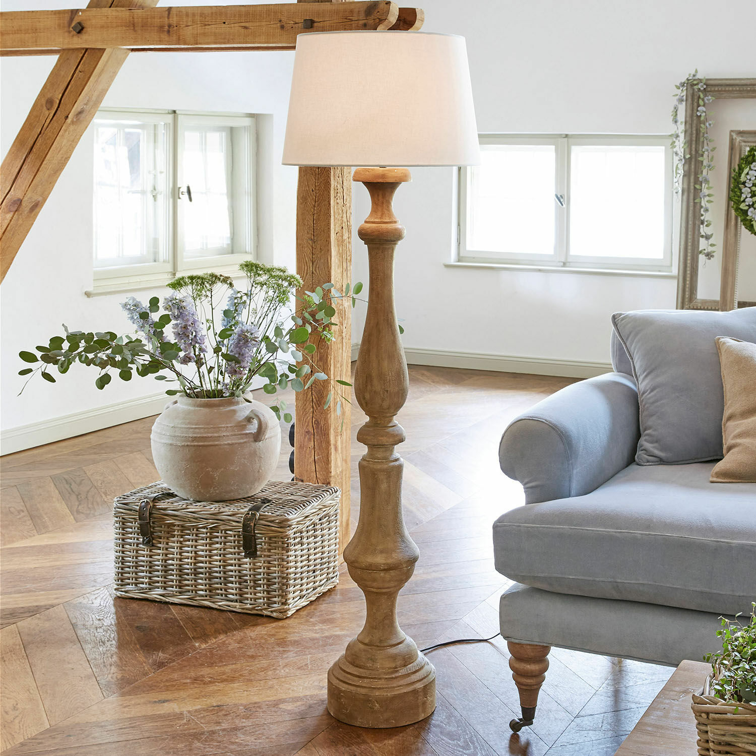 Stehlampe Etienne Holz-Stehlampe mit weissem Lampenschirm im hellen Wohnzimmer mit blauem Sofa und Weidenkorb