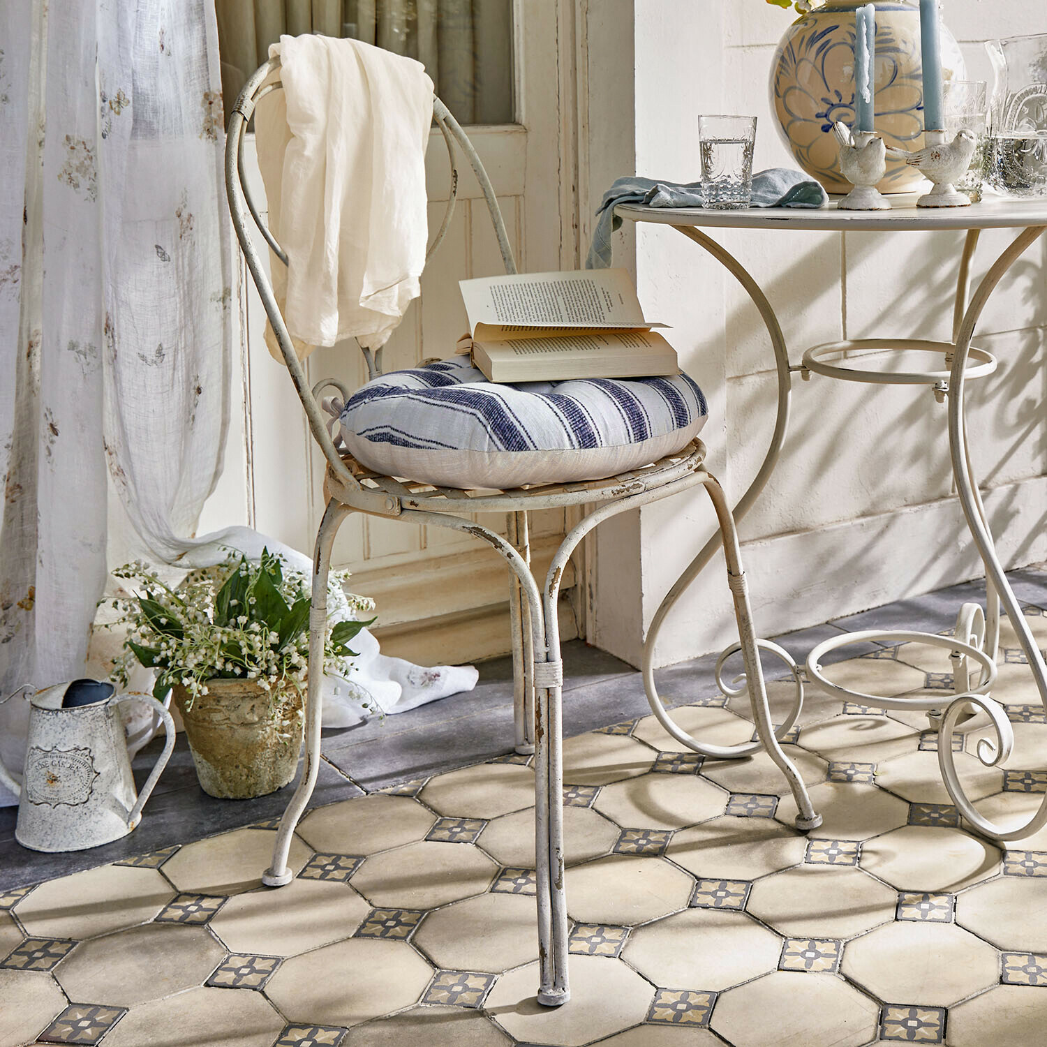 Stuhl Aube Vintage Metallstuhl mit blau-weiß gestreiftem Kissen und weissem Tuch im hellen Raum mit Fliesenboden