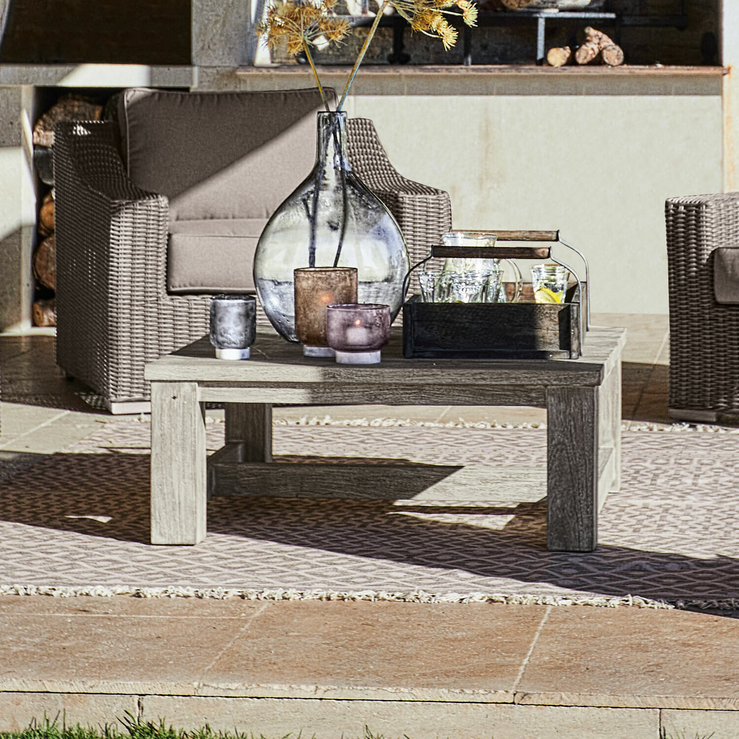 Couchtisch Malden Niedriger Holztisch auf der Terrasse mit dekorativen Kerzen und Vase, Rattan-Gartenmöbel im Hintergrund