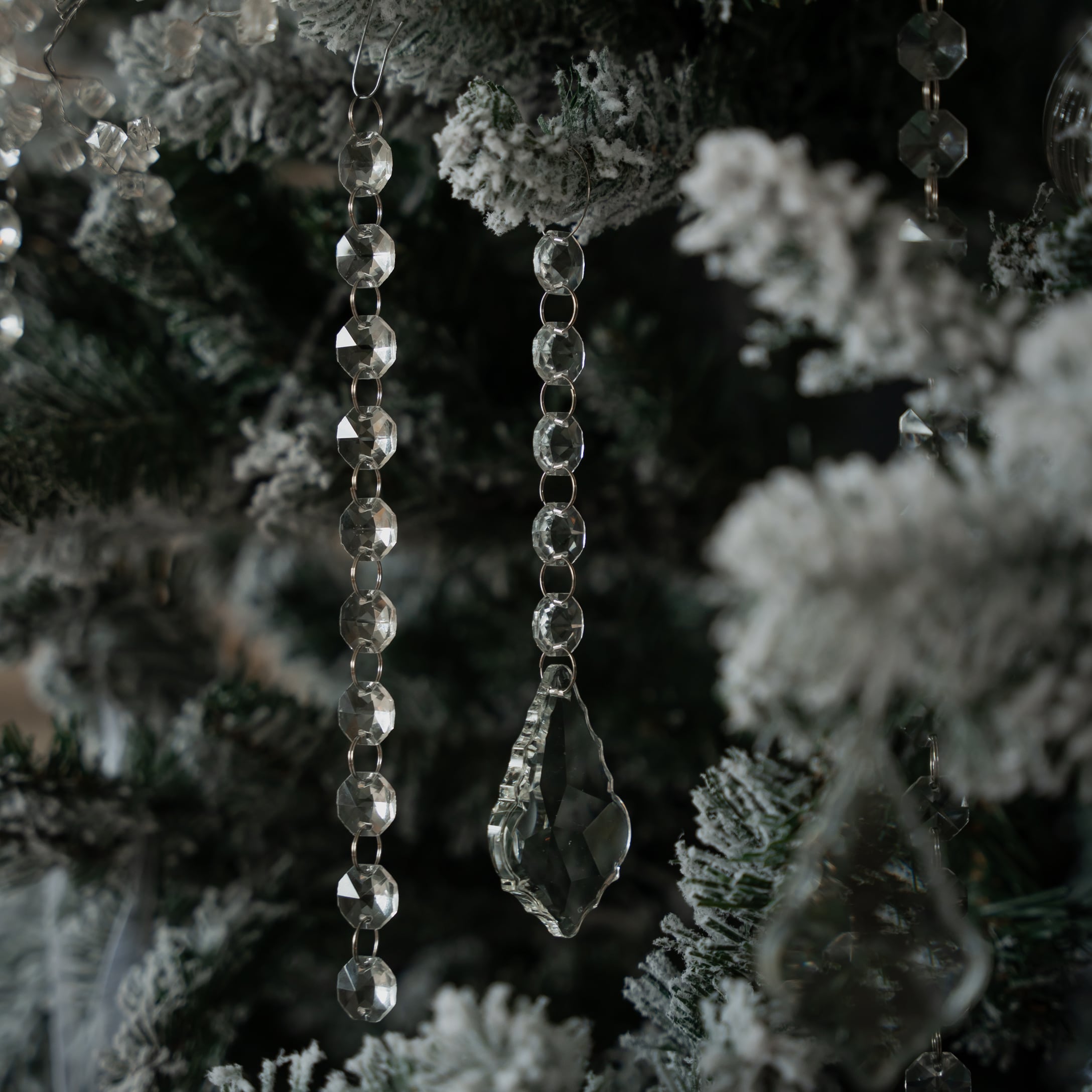 Weihnachtsschmuck aus transparenten Kristallperlen und Anhängern an schneebedeckten grünen Zweigen