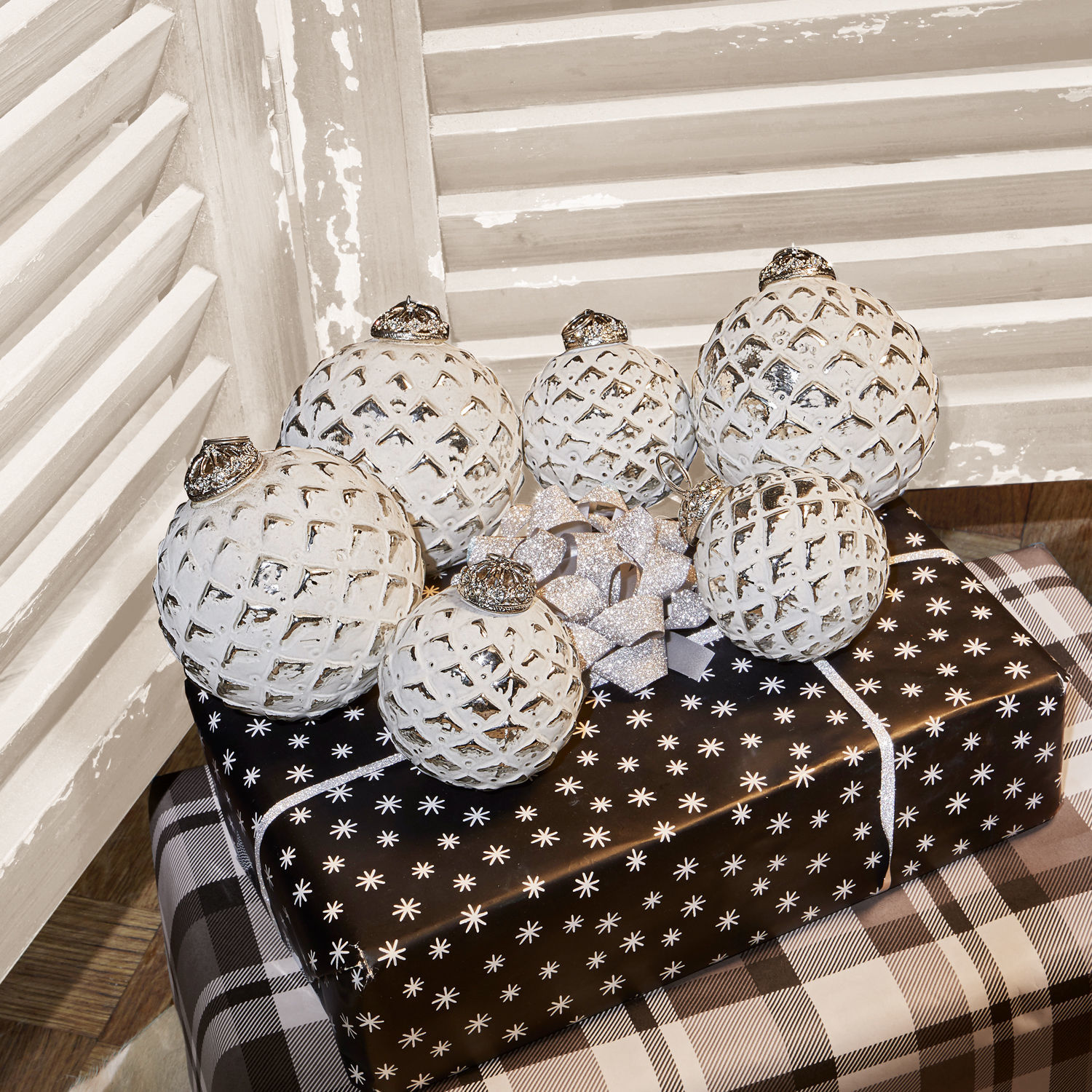 Weisse Weihnachtskugeln mit Rautenmuster auf schwarz-weiss verpackten Geschenken in rustikalem Ambiente