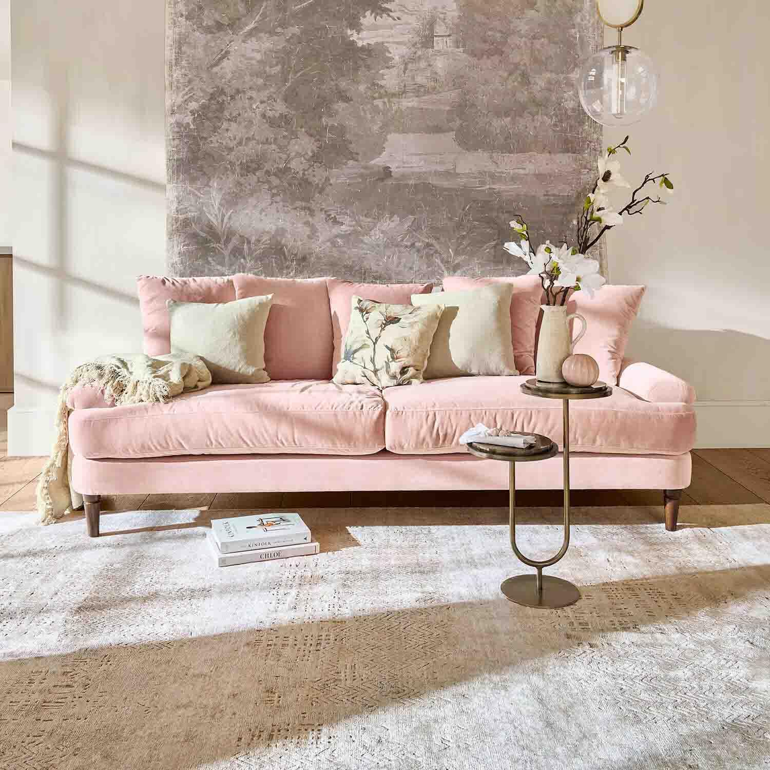 Rosa Samtsofa mit Kissen und Beistelltisch in hellem Wohnzimmer mit Wanddekoration