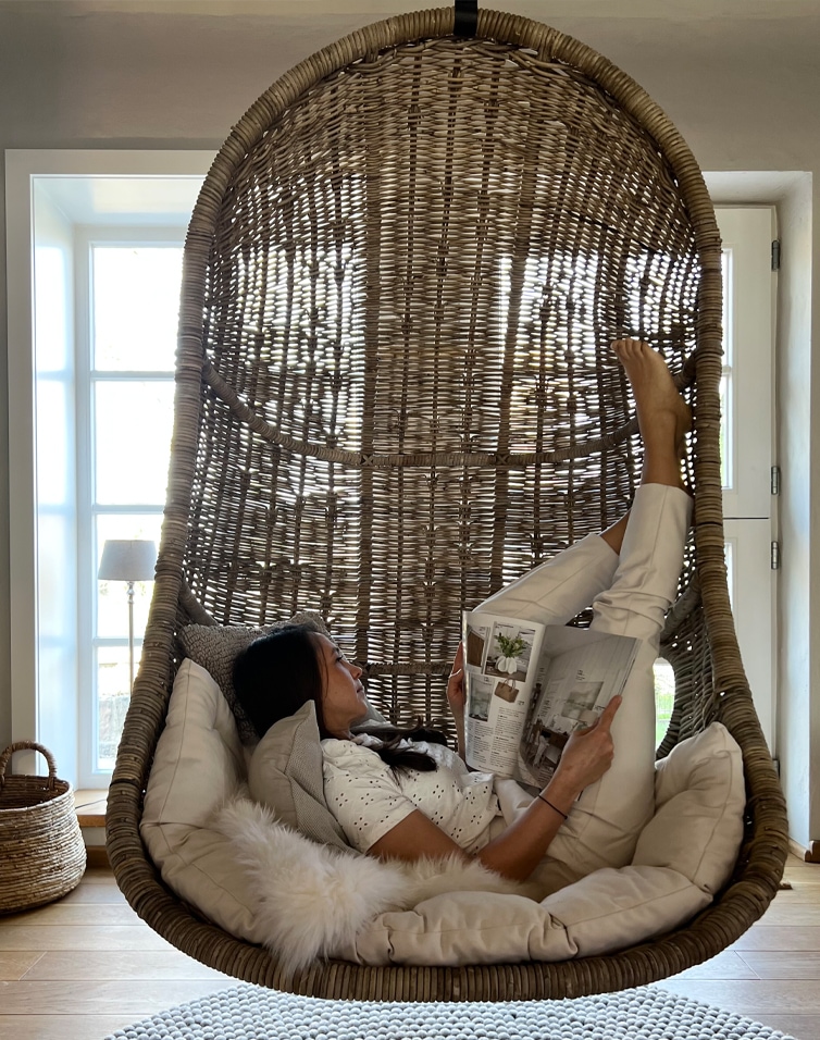 Hängesessel aus natürlichem Rattan mit weichen Kissen und Frau, die entspannt ein Buch liest