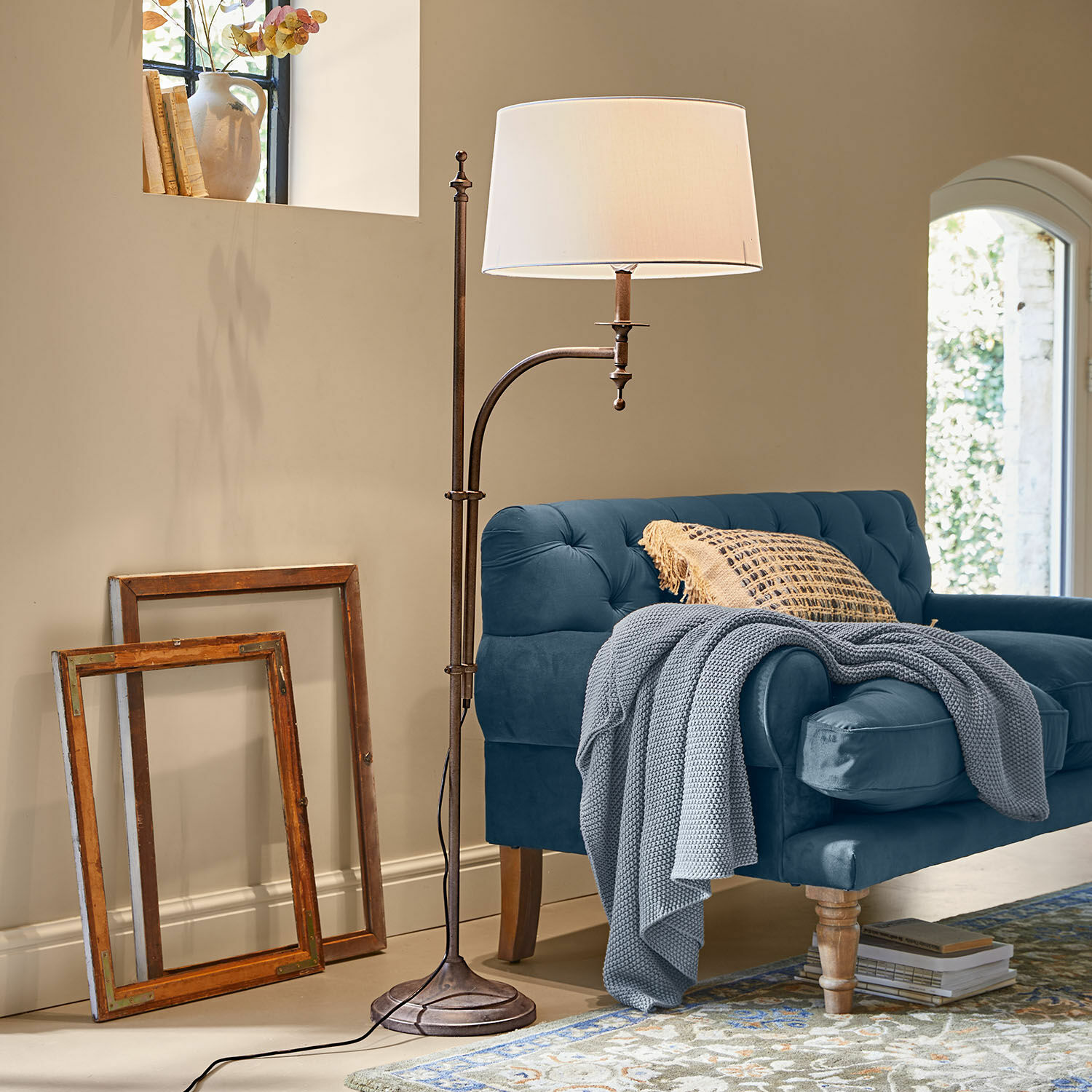Stehlampe Salvaterre Stehlampe aus Metall mit weissem Lampenschirm neben blauem Sofa und zwei Holzrahmen an der Wand.