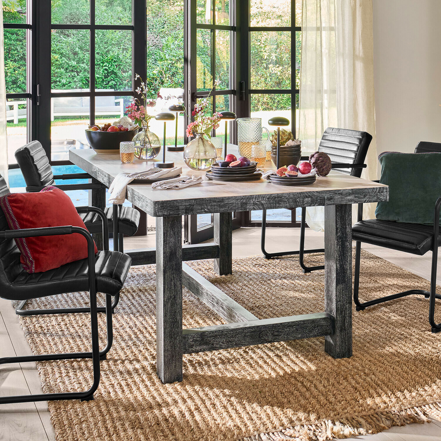 Rustikaler Holzesstisch mit schwarzen Stühlen und Dekorationen auf natürlichem Teppich in hellem Raum