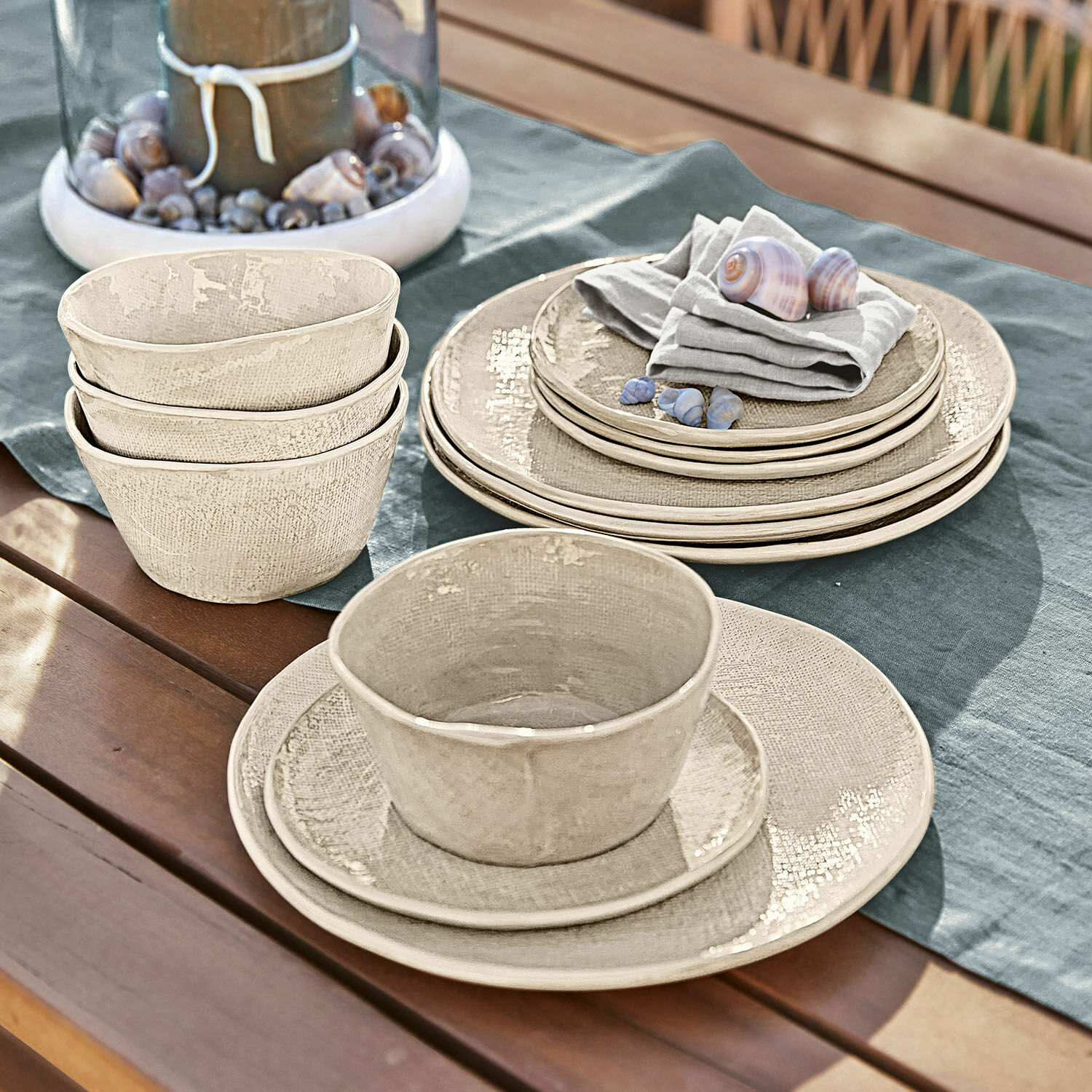 Geschirr 12er Set Luganville Beige Keramikgeschirr auf Holztisch mit Muscheln und Leinentuch für das Essen im Freien