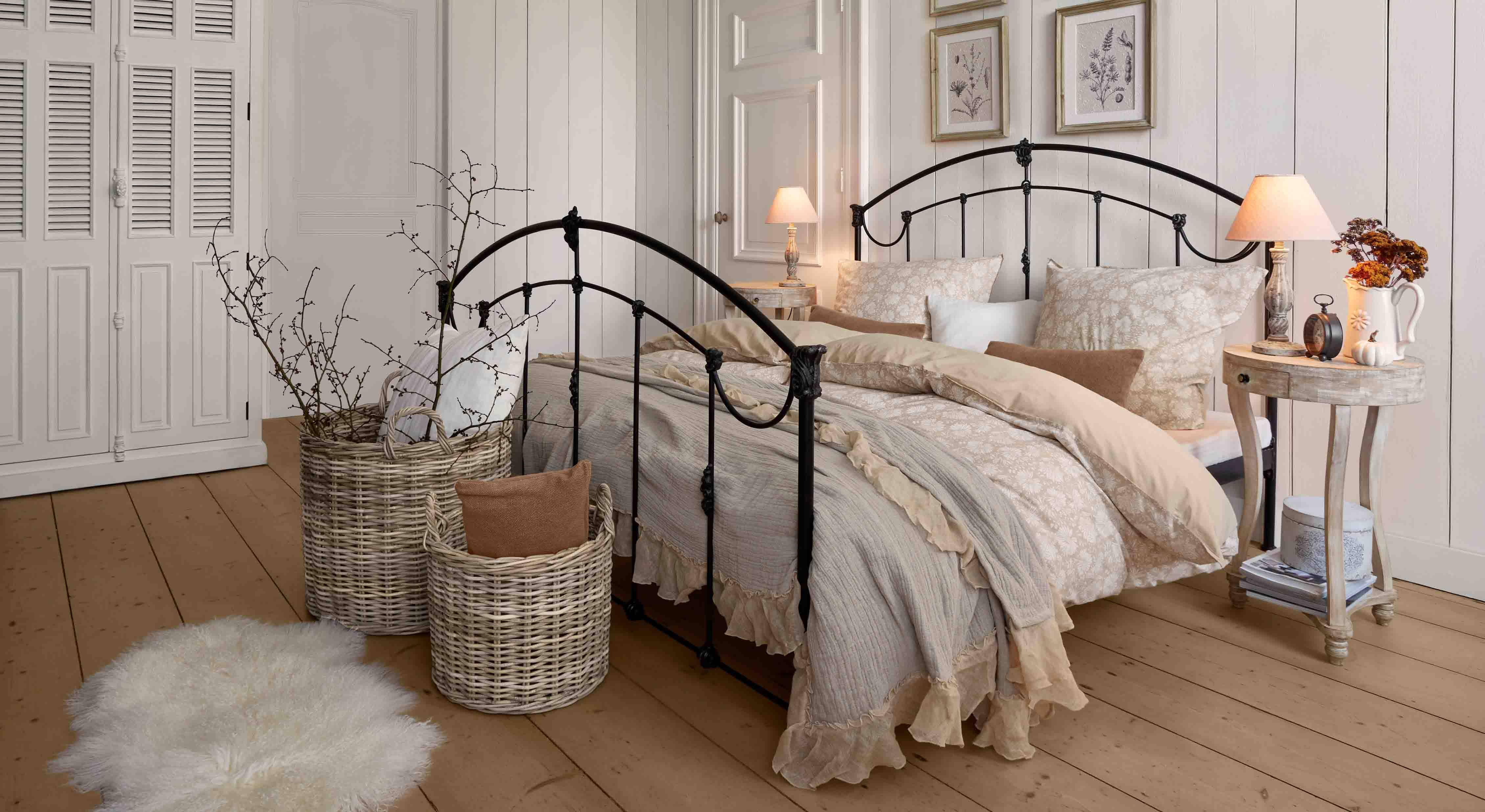 Schlafzimmer mit schwarzem Metallbett und beiger Vintage-Bettwäsche, Weidenkorb und Nachttischlampe