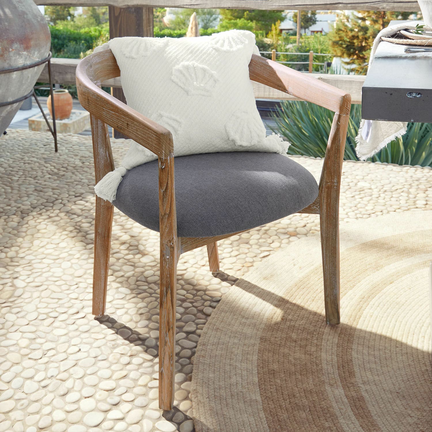 Stuhl Lunebois Stuhl aus Holz mit grauem Polstersitz und weissem Dekokissen auf sonniger Terrasse