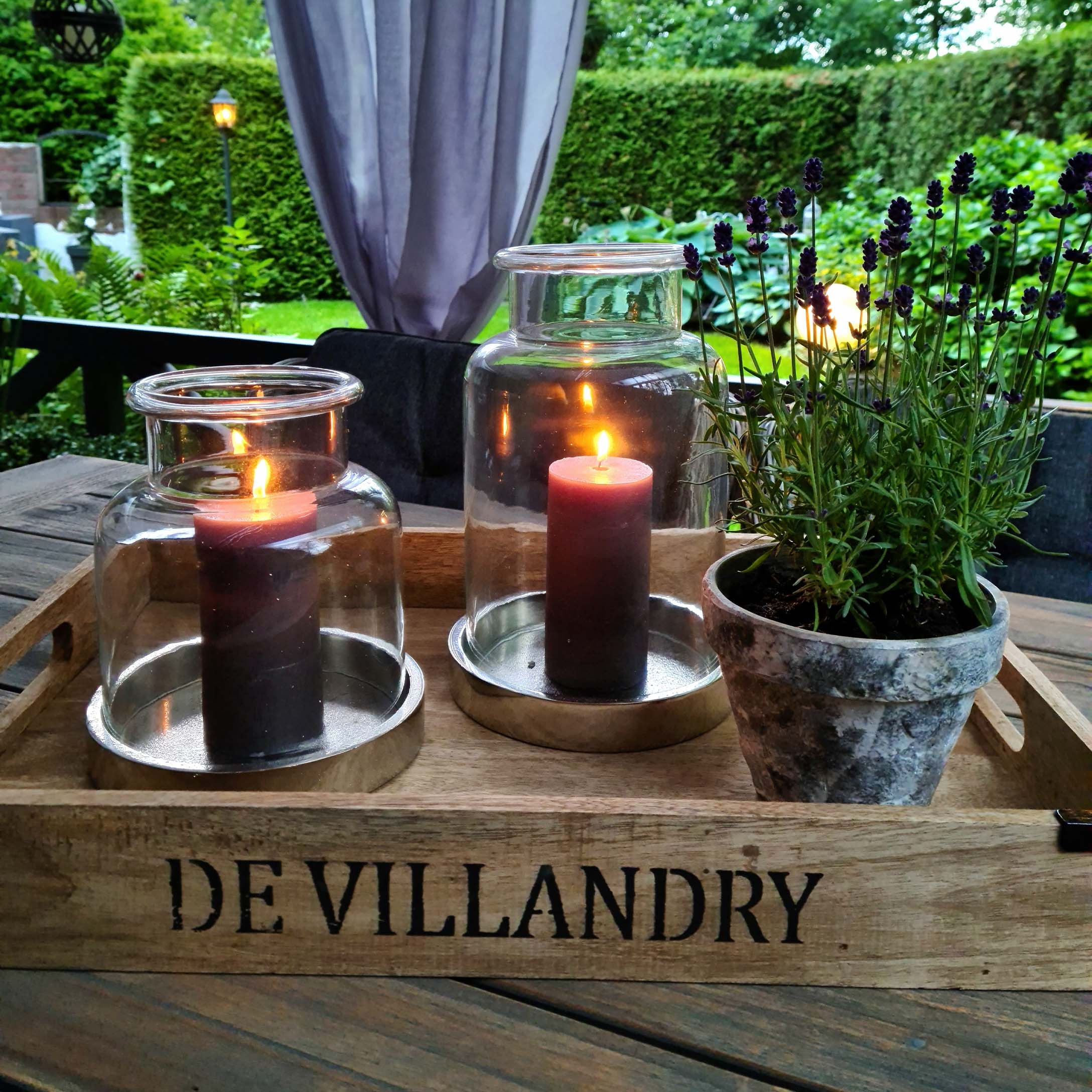 Holztablett mit zwei Glaslaternen und einem Lavendeltopf auf dem Holztisch im Garten