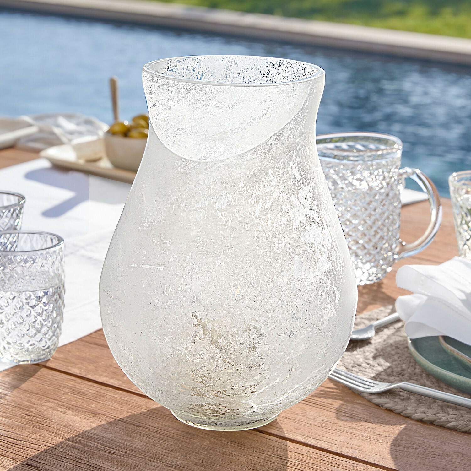 Transparenter Krug aus mattiertem Glas auf Holztisch am Pool, stilvolles Trinkgefäß