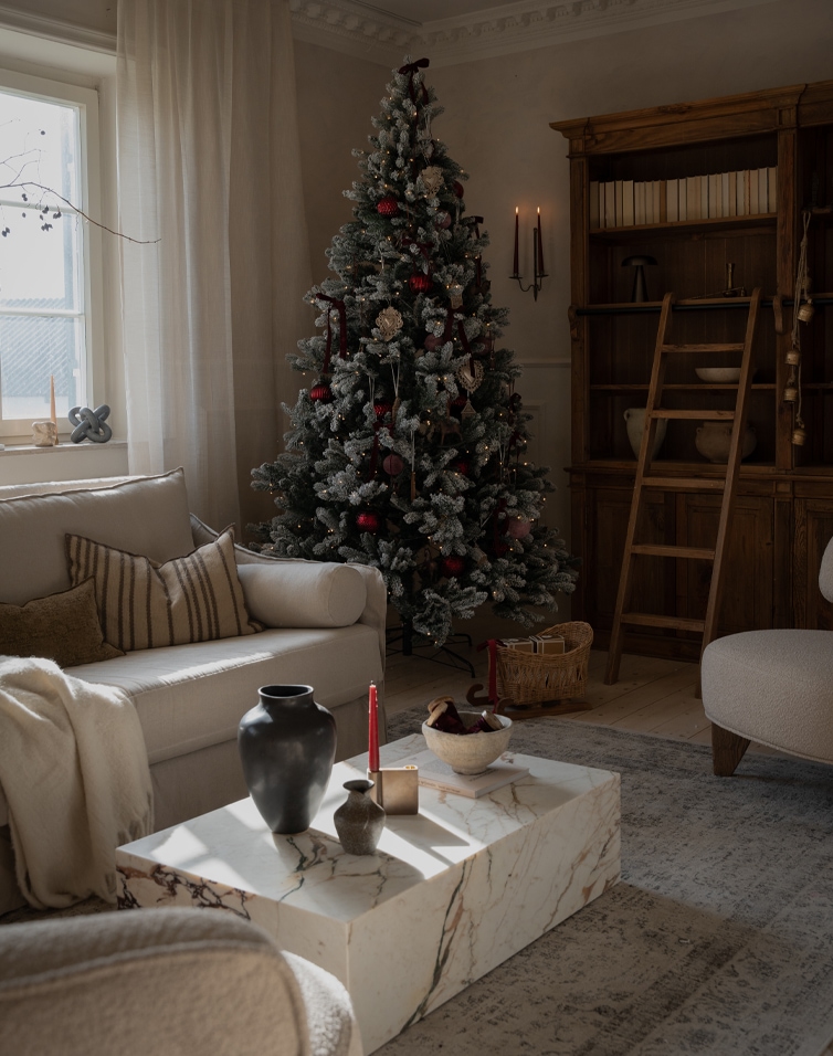 Gemütliches Wohnzimmer mit künstlichem Weihnachtsbaum in Grün-Rot und einem Marmortisch als Salon- oder Sofatisch