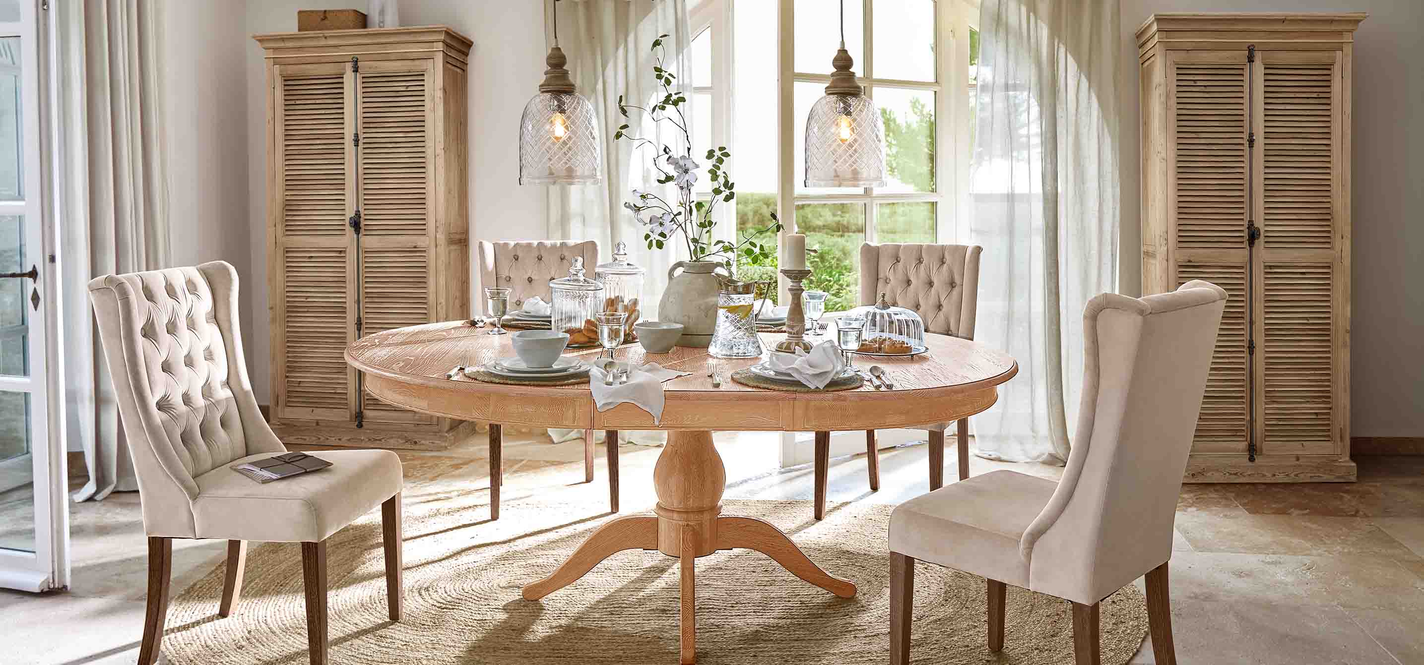 Esszimmer mit rundem Tisch aus hellem Holz und beige gepolsterten Stühlen im Vintage-Stil