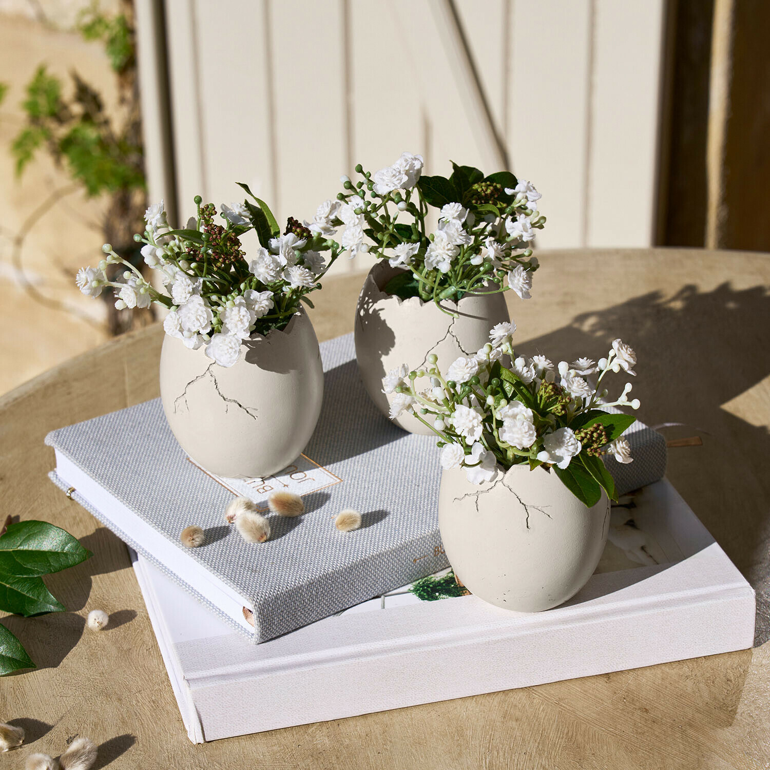 Deko-Ei 3er Set Waverlye Drei weisse Keramikvasen in Ei-Form mit weissen Blumen auf Holztisch mit Büchern
