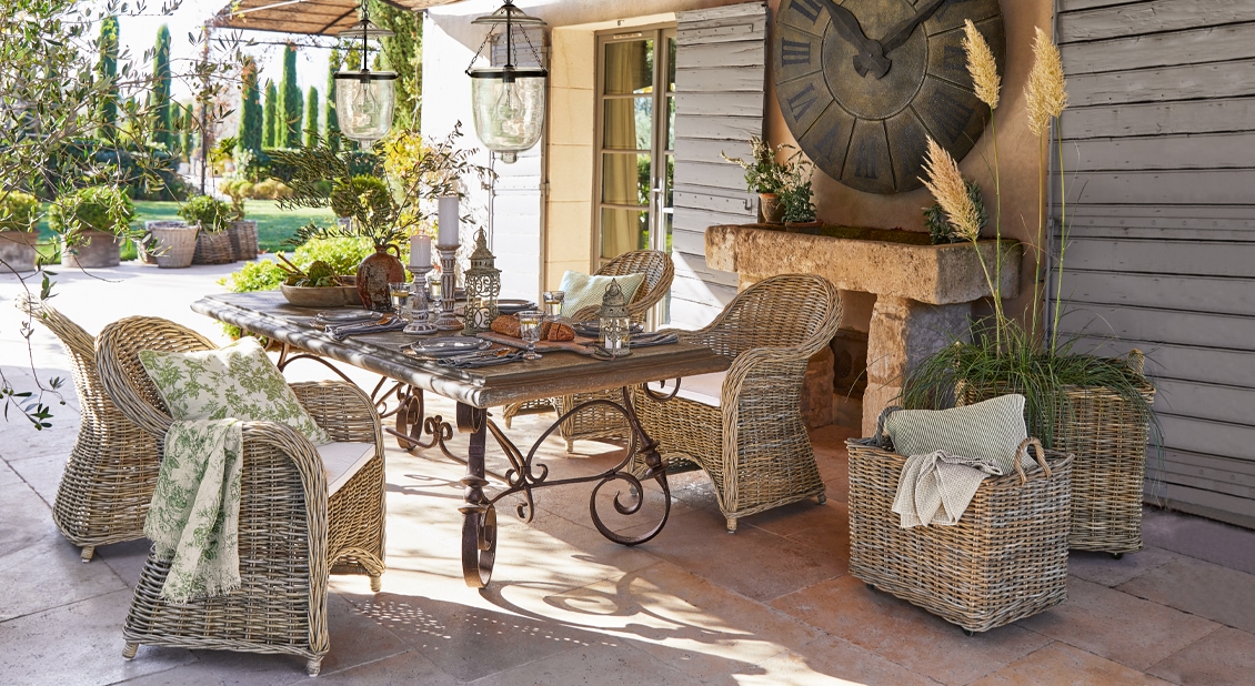 Gartenmöbel-Set aus natürlichem Rattan mit Metalltisch und Dekorationen auf sonniger Terrasse