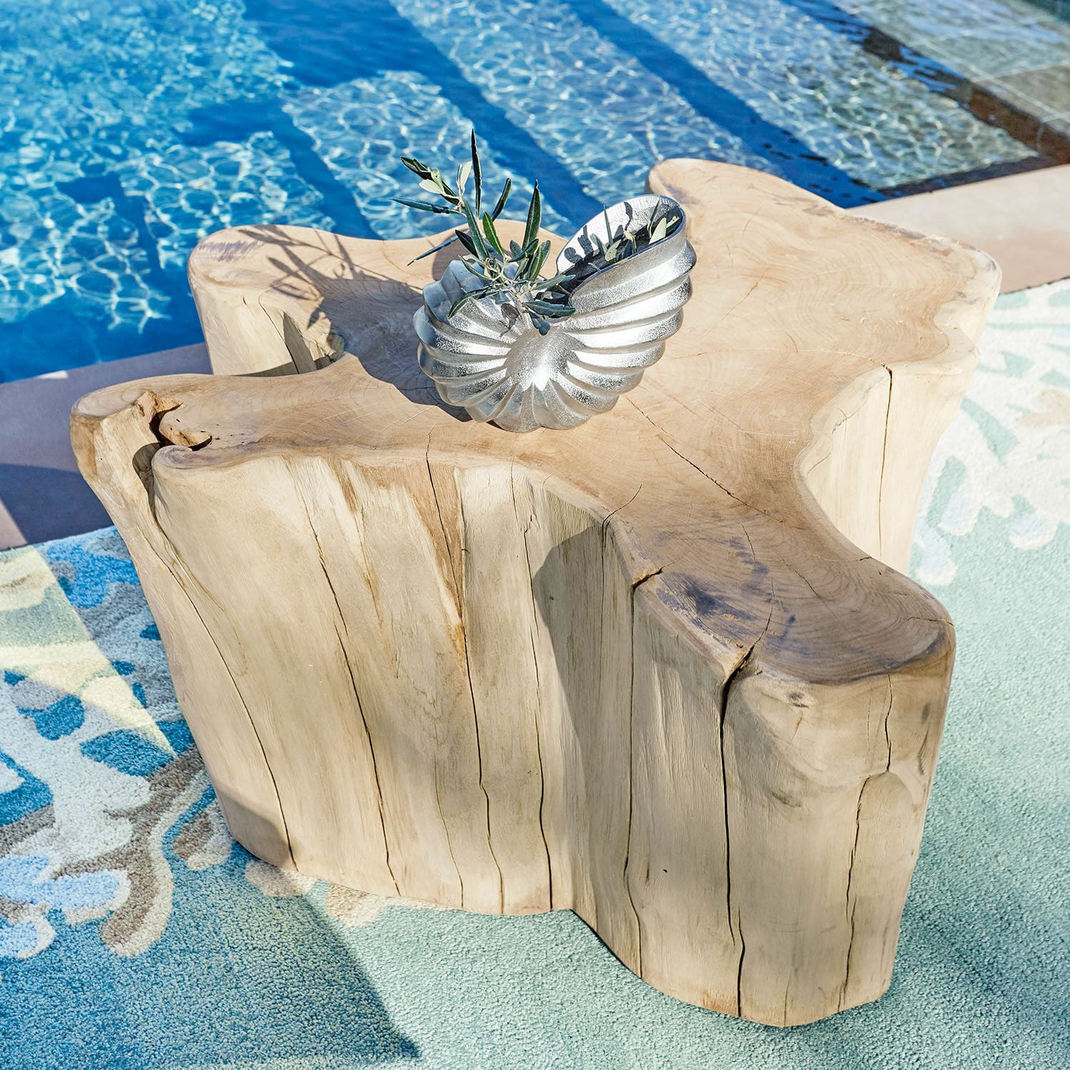 Couchtisch Dorlancourt Massiver Holztisch mit natürlicher Form neben dem Pool auf dem Teppich, silberne Dekoration darauf