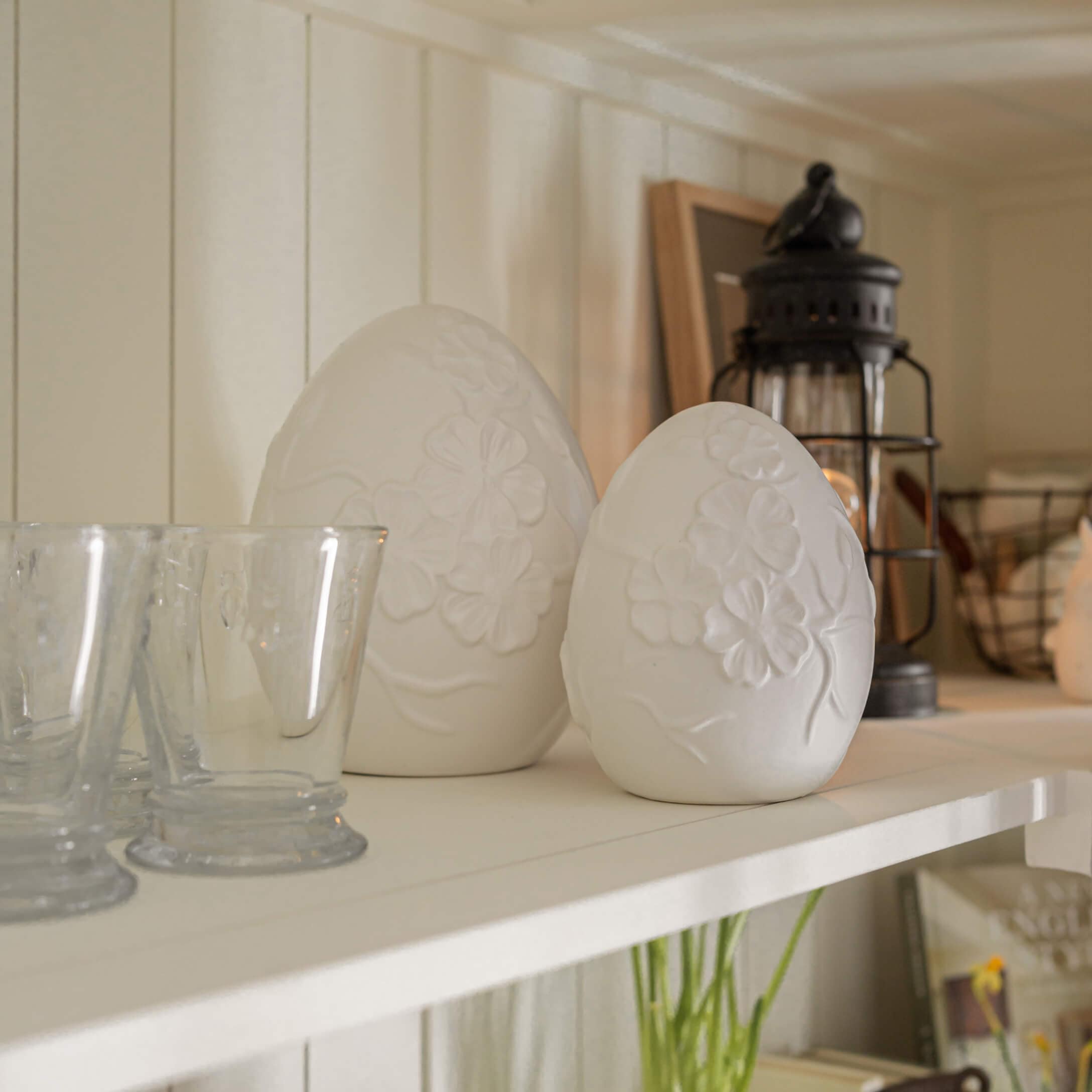 Weiße Alabaster-Deko-Eier mit Blumenmuster auf rustikalem Regal platziert