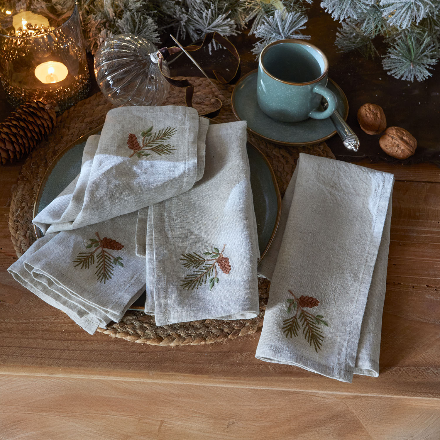 Leinenservietten mit bestickten Tannenzapfen und Zweigen auf Holztisch mit Weihnachtsdeko