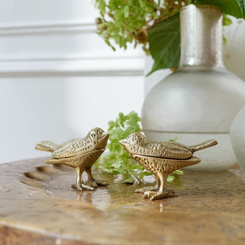 Zwei dekorative Vogelfiguren aus goldenem Metall auf einem Holztisch als Wohnaccessoire