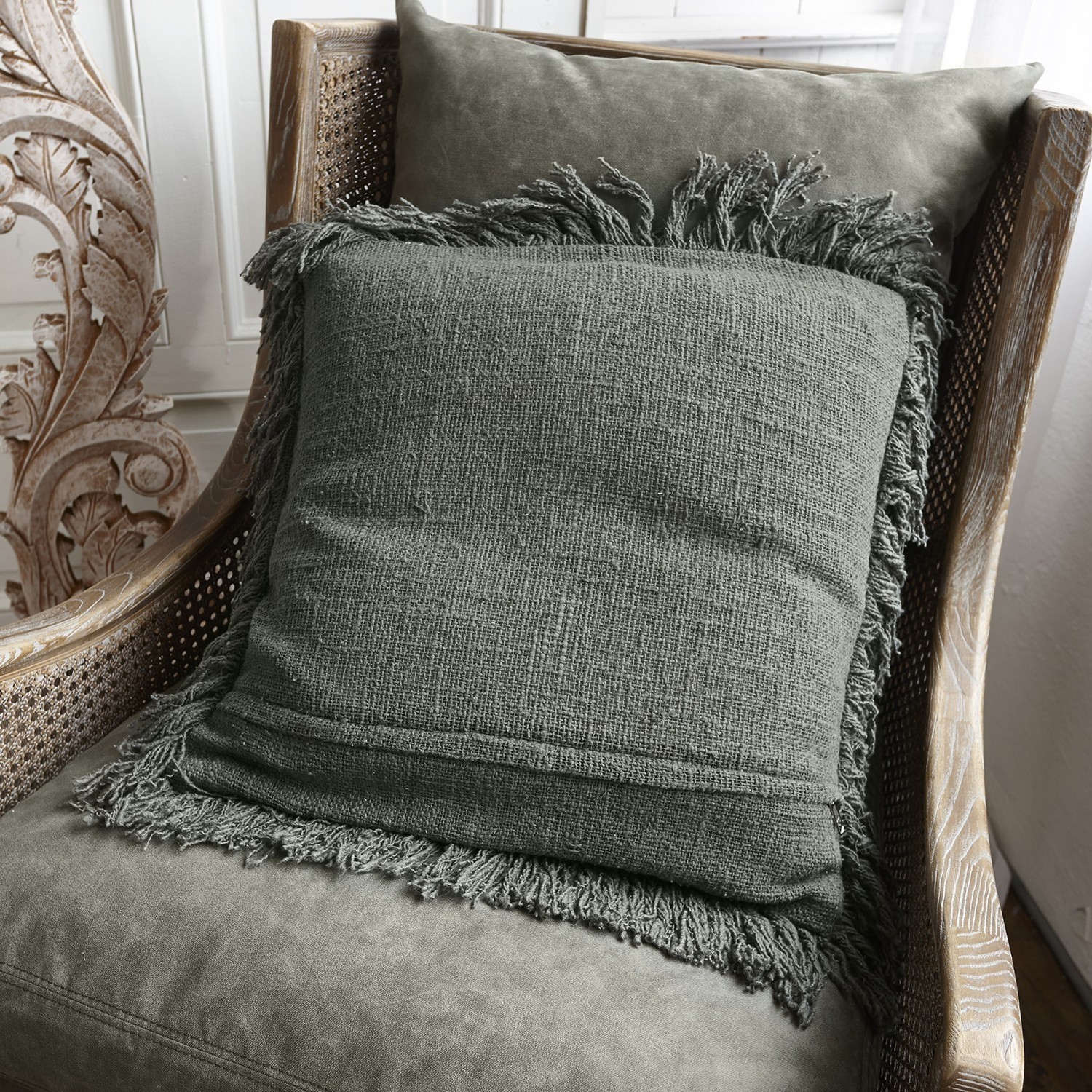 Kissen Greenly Grünes Dekokissen mit Fransen auf einem weichen Holz-Rattan-Sessel im Wohnzimmer