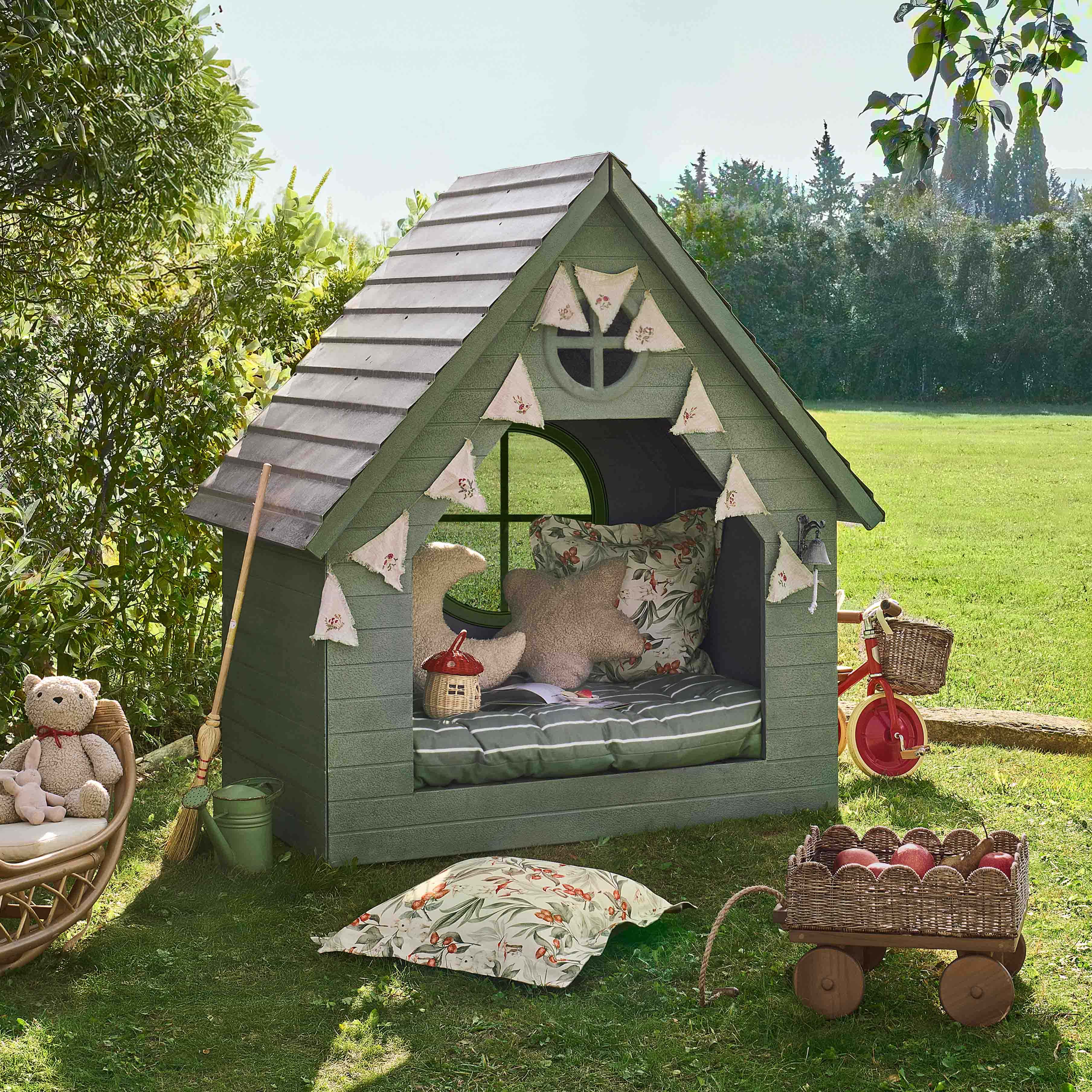 Grünes Holzspielhaus mit dekorativen Kissen und Wimpelgirlande, ideal für Kinderspiel im Garten.