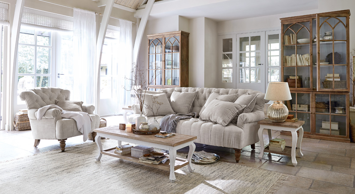 Gemütliches Landhaus-Wohnzimmer mit beigem Stoffsofa, Sessel, Holzmöbeln und hellem Teppich
