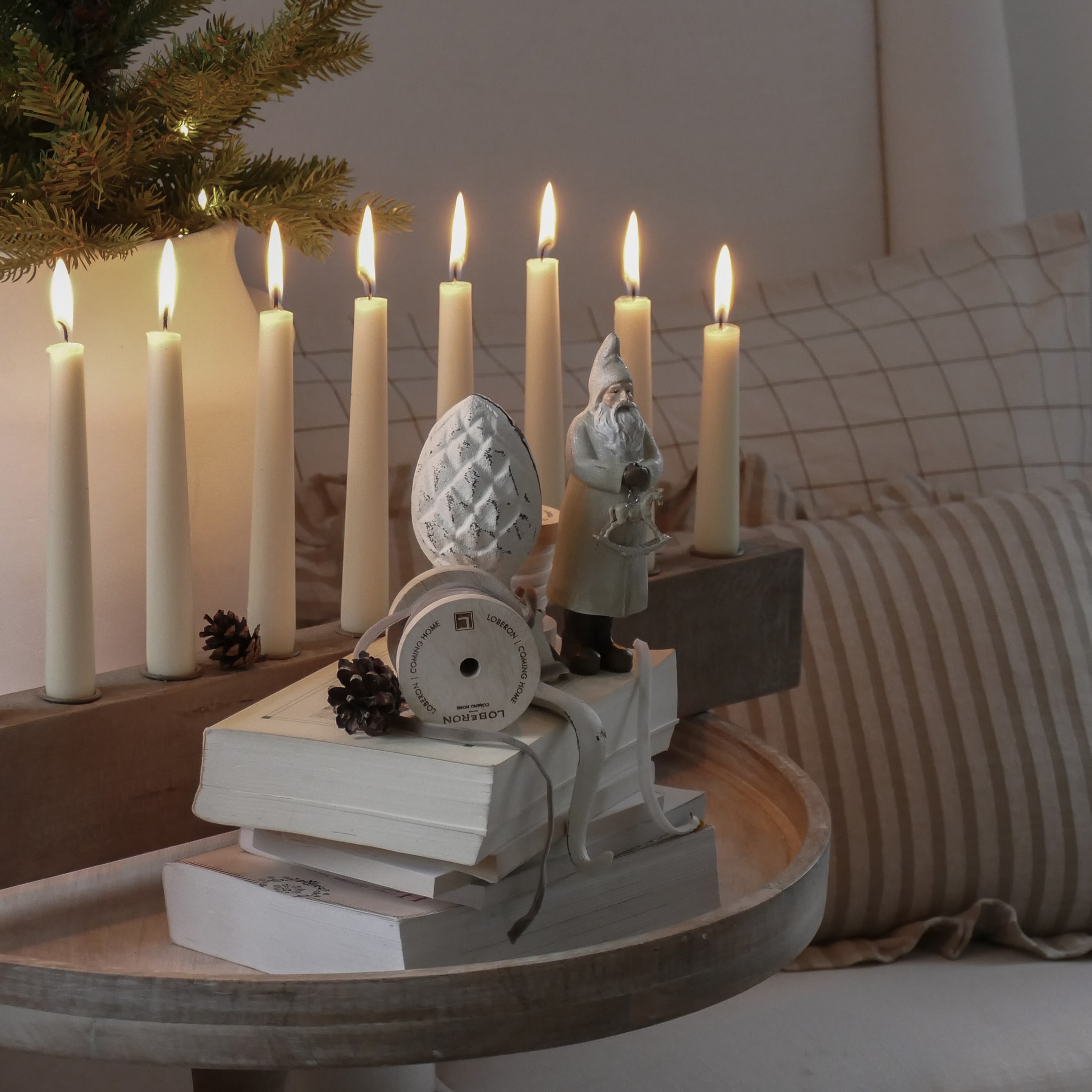 Weihnachtsdekoration mit Weihnachtsmannfigur, brennenden Kerzen und Büchern auf hellem Holztablett