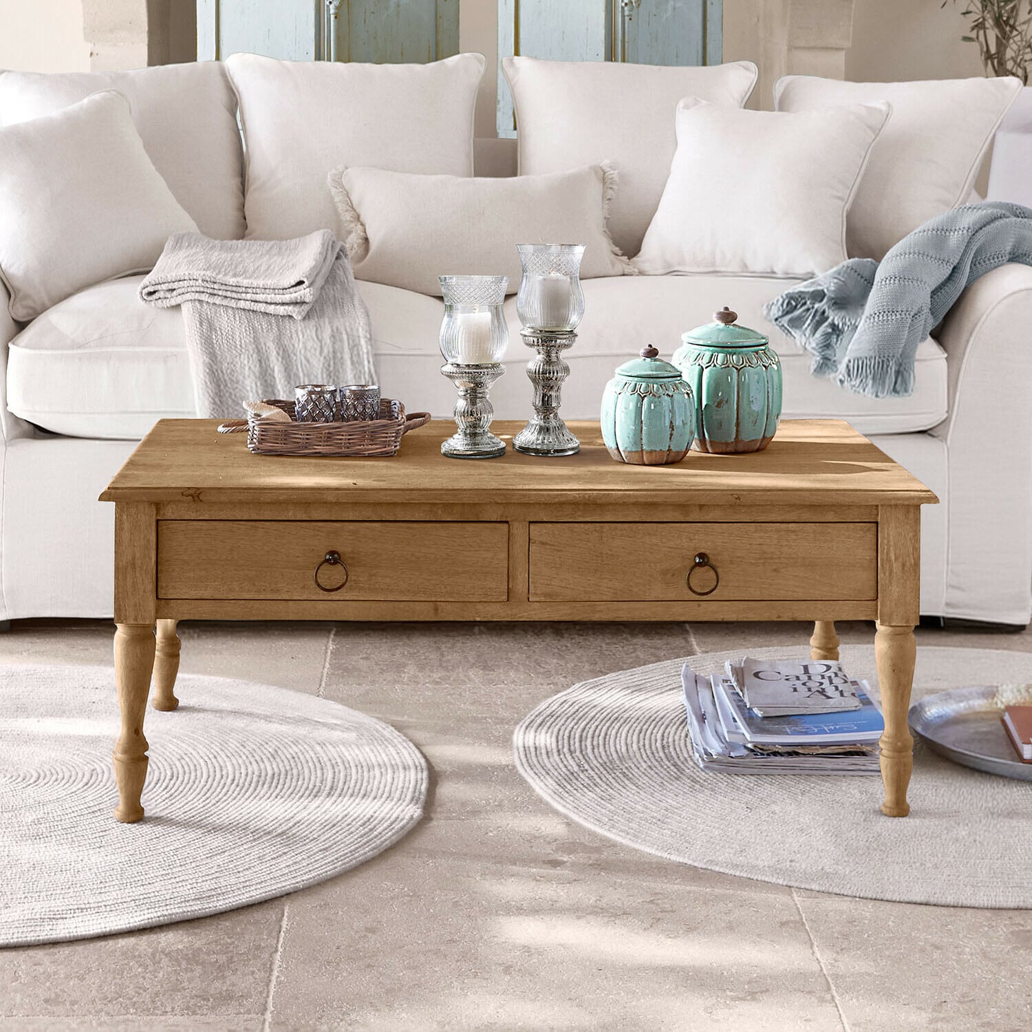Holz-Couchtisch mit Schubladen vor hellem Sofa, dekorative Kerzen und Decken darauf
