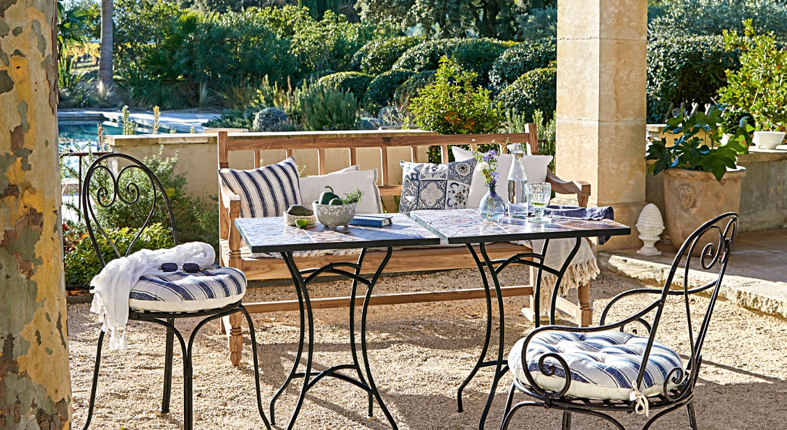 Gartenmöbel-Set mit Metallstühlen und Holzbank auf Terrasse mit gestreiften Kissen und Tisch mit Platten