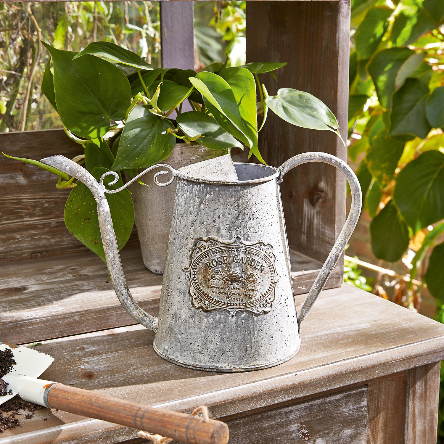 Giesskanne Rose Garden Vintage Metallgiesskanne mit Rose-Garden-Schriftzug auf Holztisch im Garten