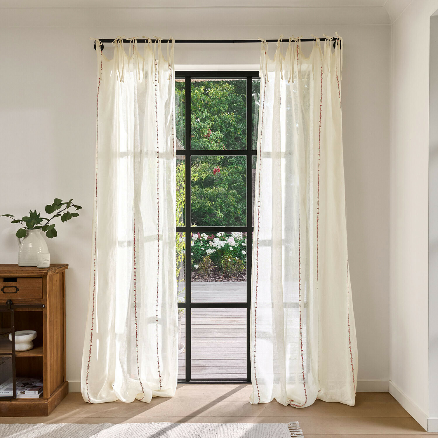 Transparente cremefarbene Vorhänge mit feinem rotem Muster, leichter Stoff vor großem Fenster