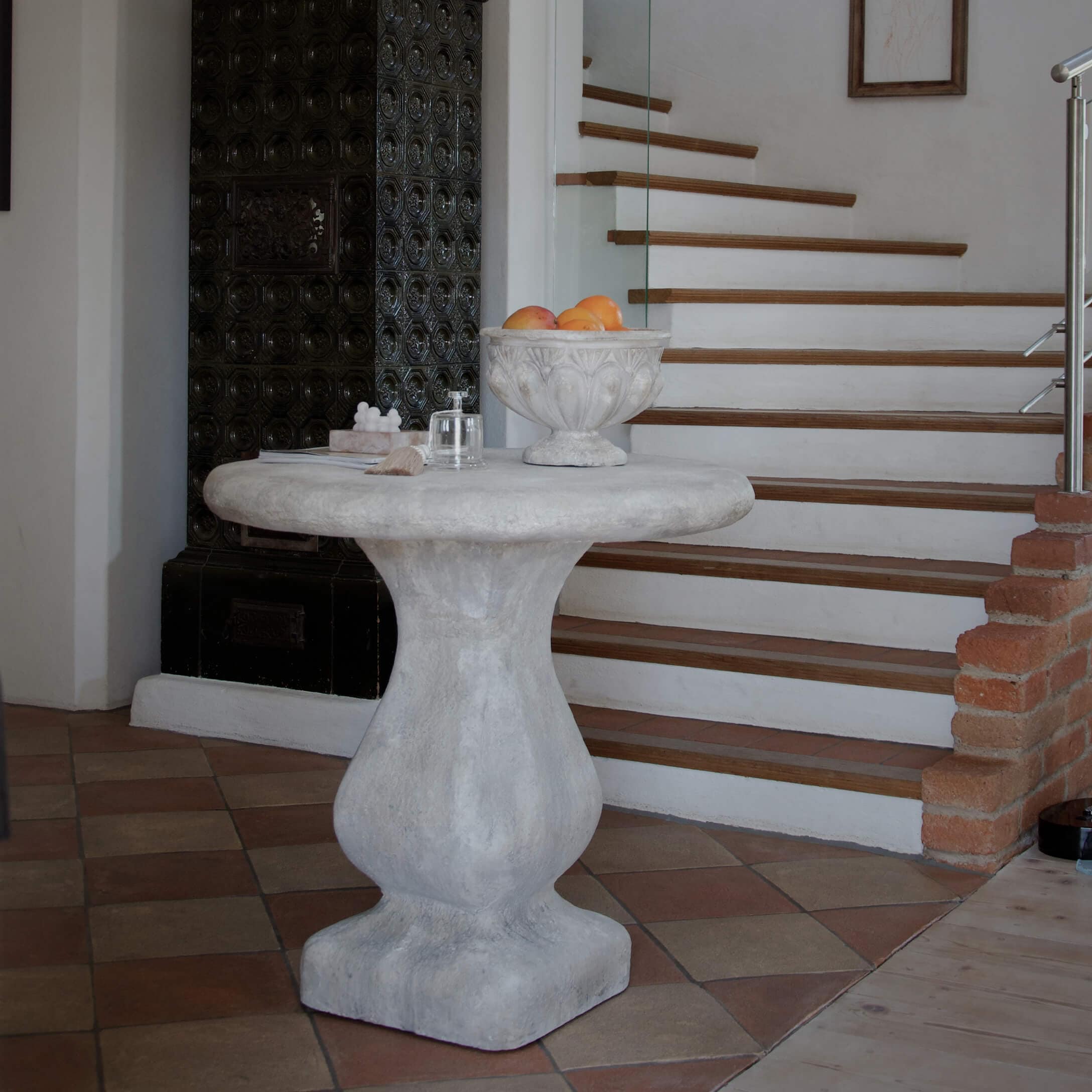 Runder grauer Betontisch neben Treppe, dekorative Schale mit Früchten auf der Tischplatte