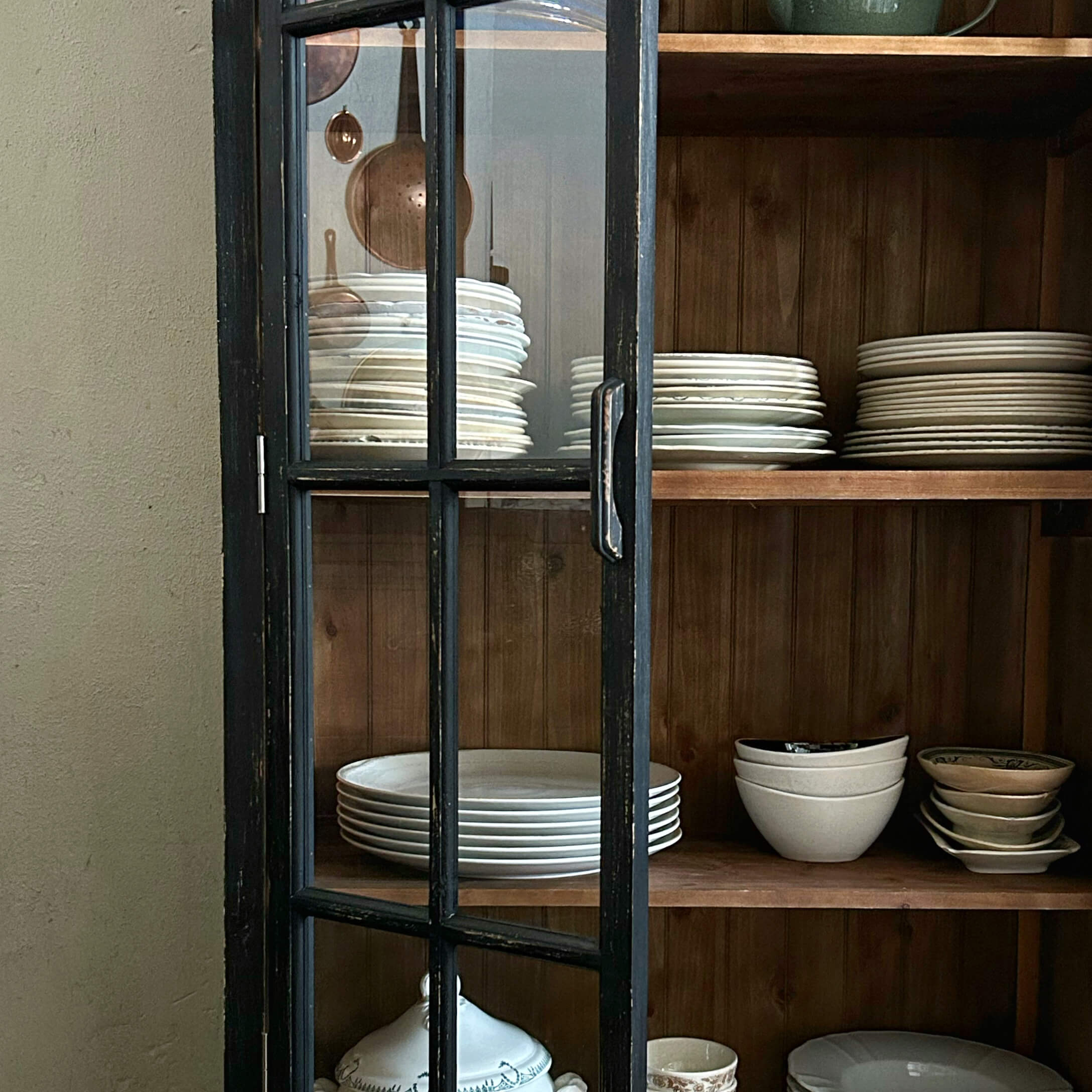 Schwarze Holzschranktür mit Glas, innen weiße Teller und Schalen auf Holzregalen