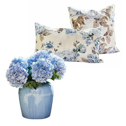 Blaue Hortensien in blauer Keramikvase mit zwei Kissen im Blumenmuster