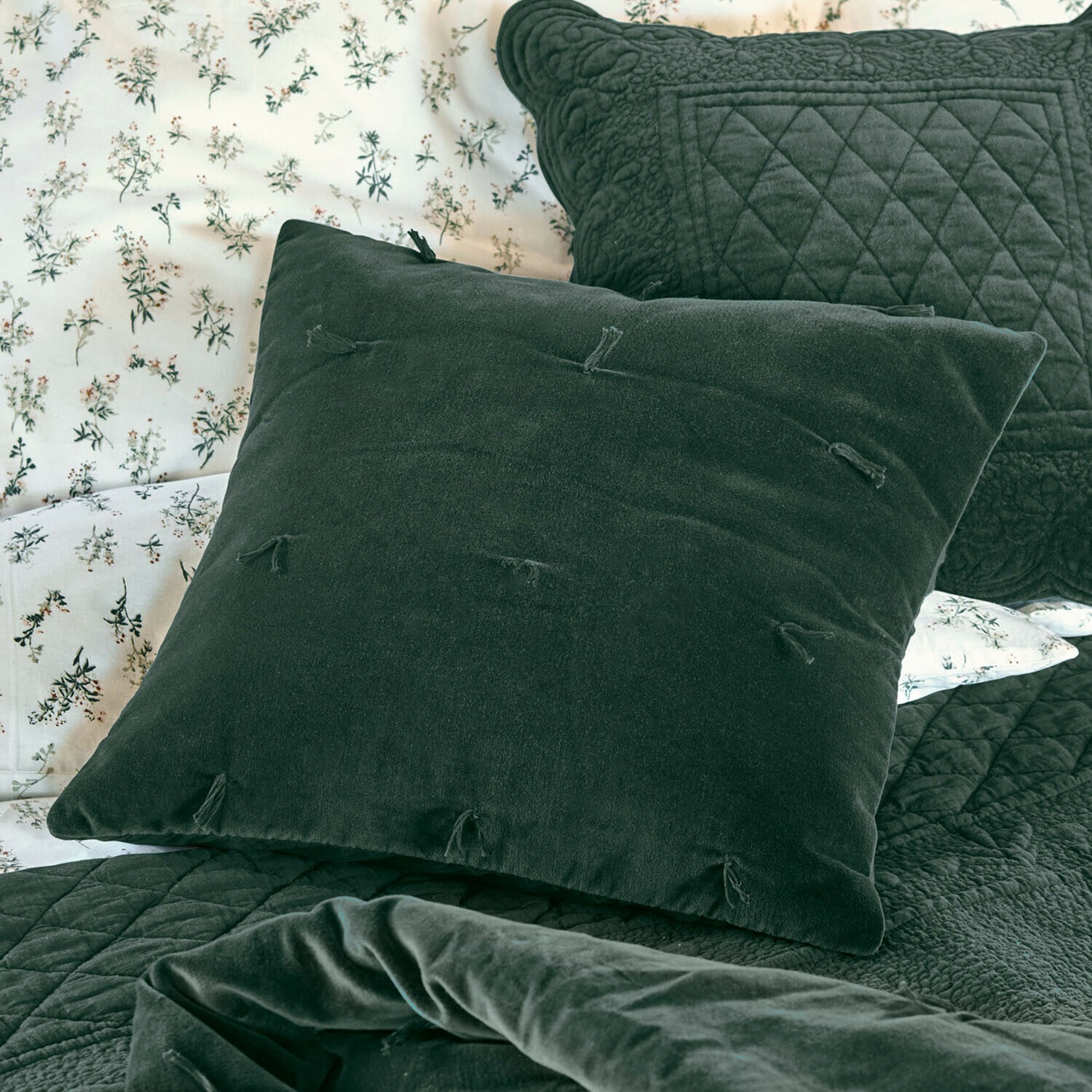 Kissen Orélisse Grünes Samtkissen mit Quasten auf Bett mit gesteppter Decke und floralem Bettbezug