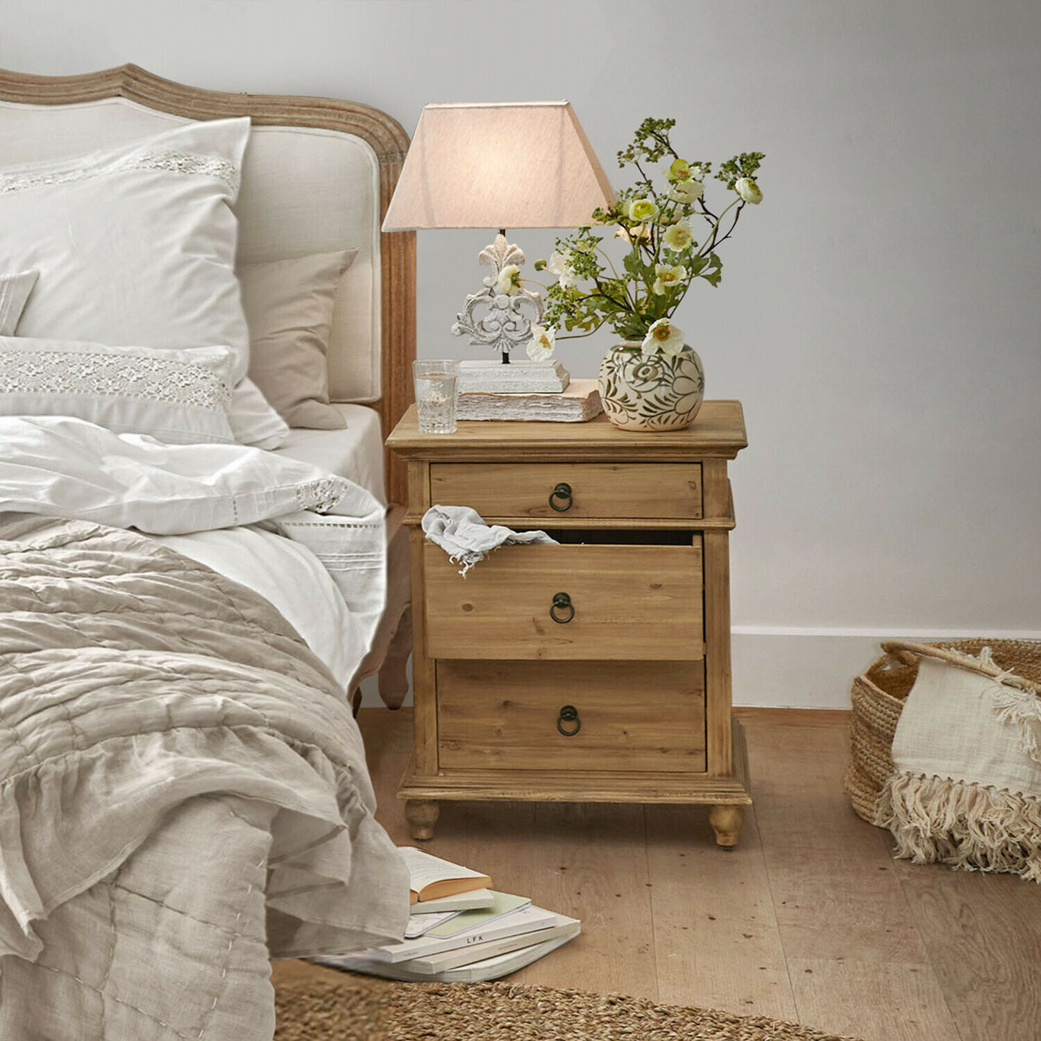 Nachttisch aus Holz mit drei Schubladen in Naturfarbe neben Bett mit weisser Bettwäsche
